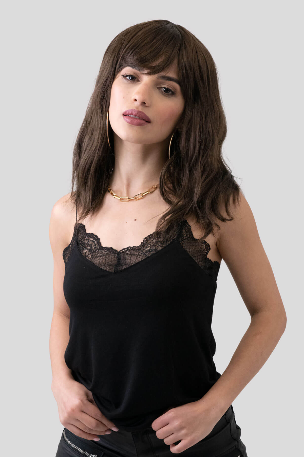 Woman wearing a black lace-trimmed top against a gray background. Long brown wavy bob (lob) wig: Lottie