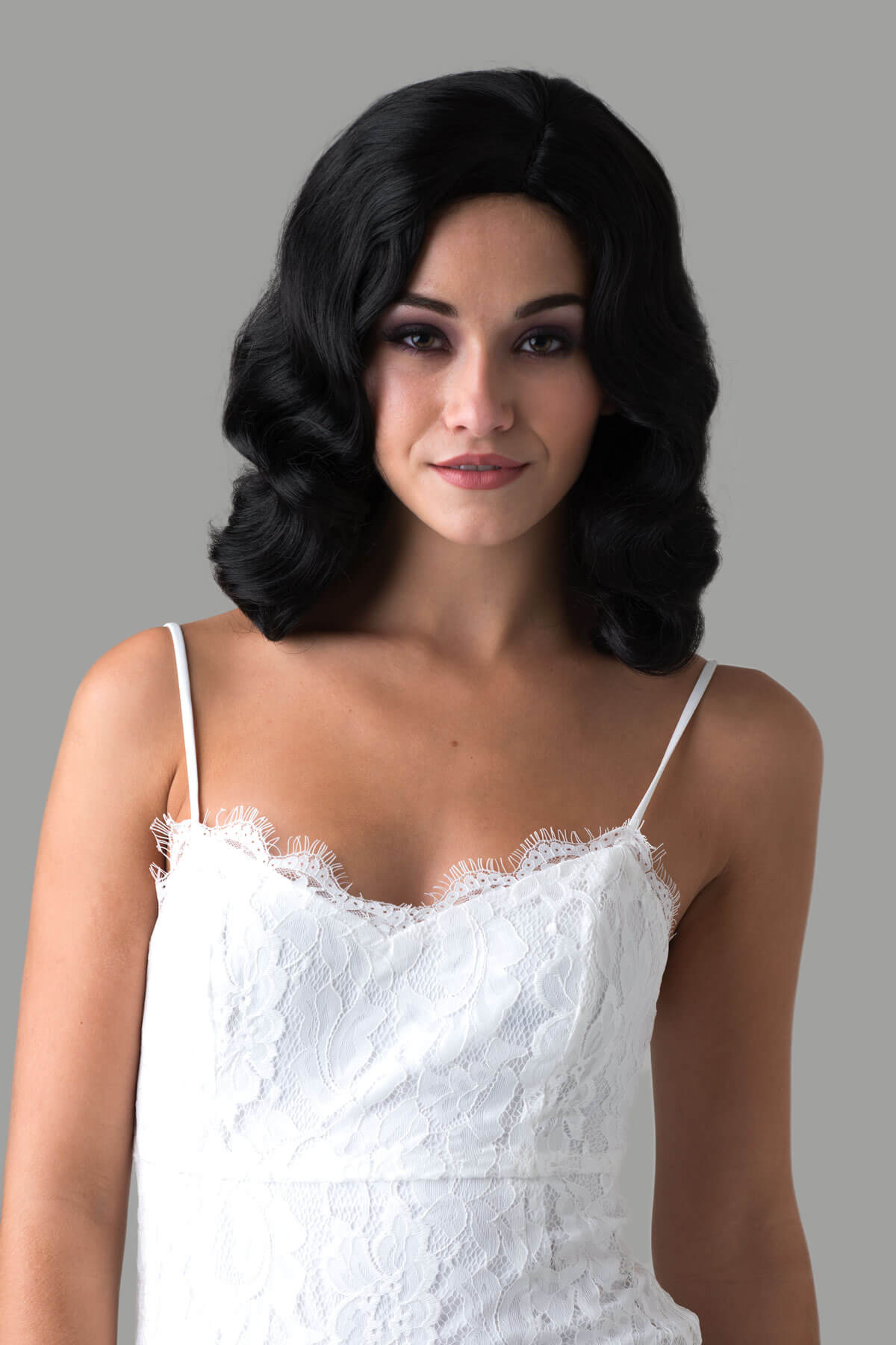 Woman wearing a white lace dress with a gray background. Black 40s style wig with beautiful marcel waves: Dita