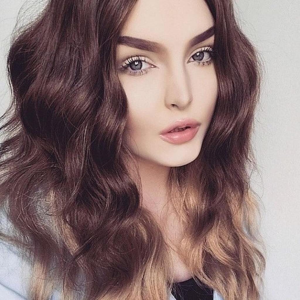 Close-up of a person with wavy brown hair on a light background. Dip dye chocolate brown and honey blonde wig long wavy wig with no fringe: Genevieve