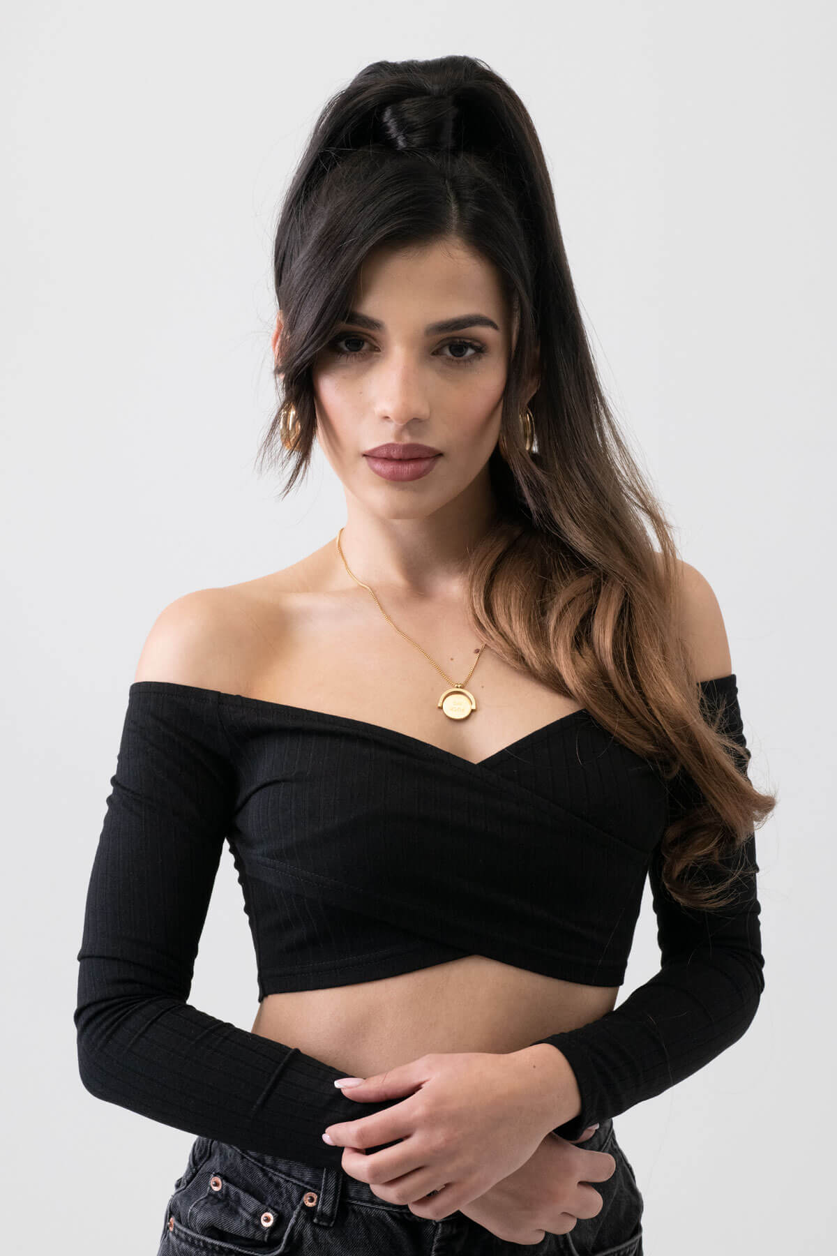 Woman wearing a black off-shoulder top against a white background. Long ponytail extension with soft waves: Sophie brown to blonde ombre 4TN27