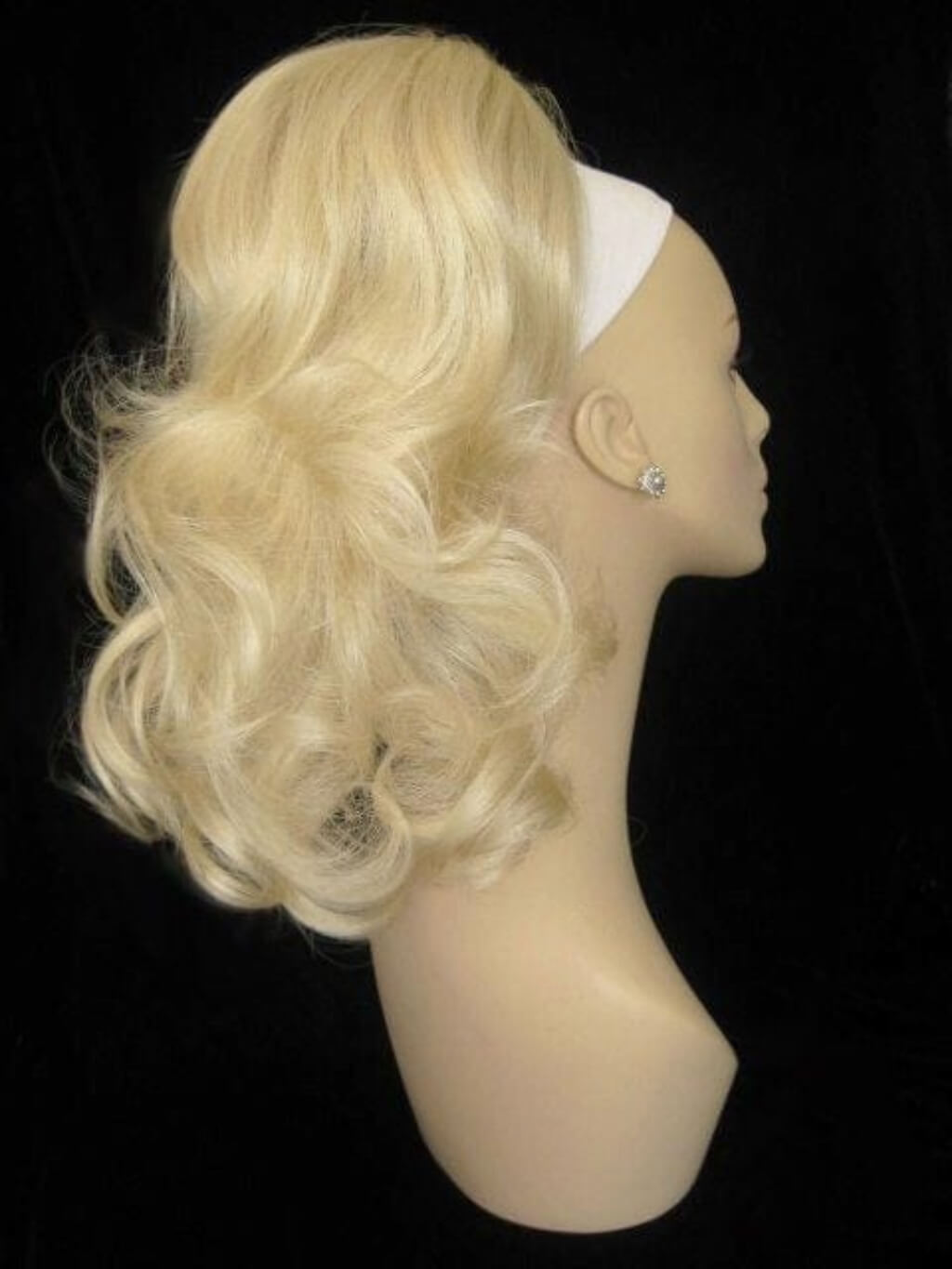 Blonde wig on a mannequin head against a black background. Curly ponytail extension clip-on hairpiece: Tulisa blonde 613