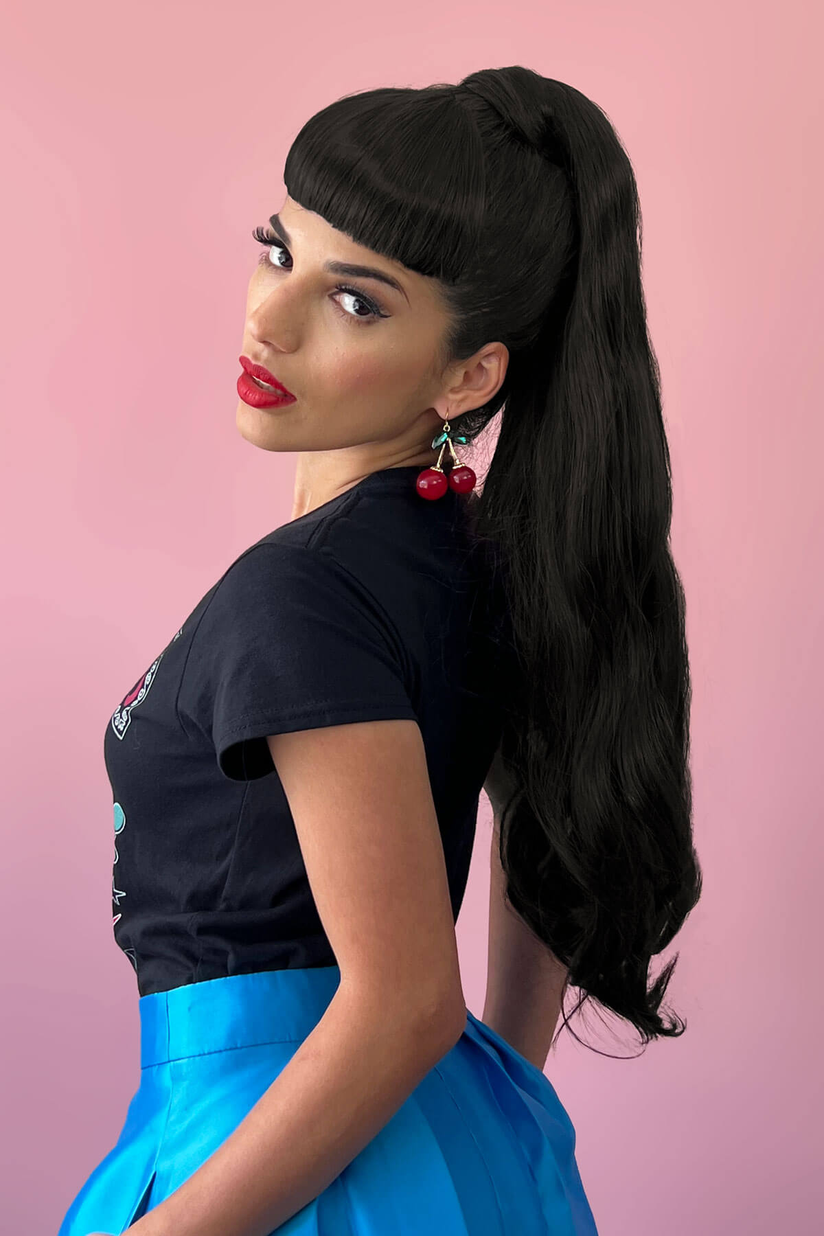 Woman with long black hair styled in a high ponytail, wearing a black top and blue skirt on a pink background. Long ponytail extension with soft waves: Sophie black 1b