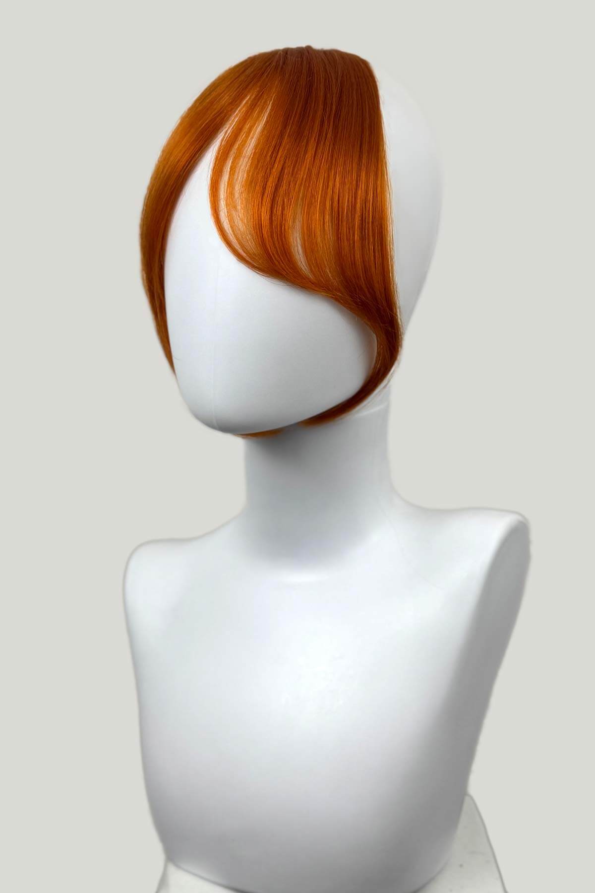 Mannequin head with a ginger hairpiece on a white background. Clip in fringe hairpiece/clip-in curtain bangs, with long, face framing wisps: Sabrina ginger
