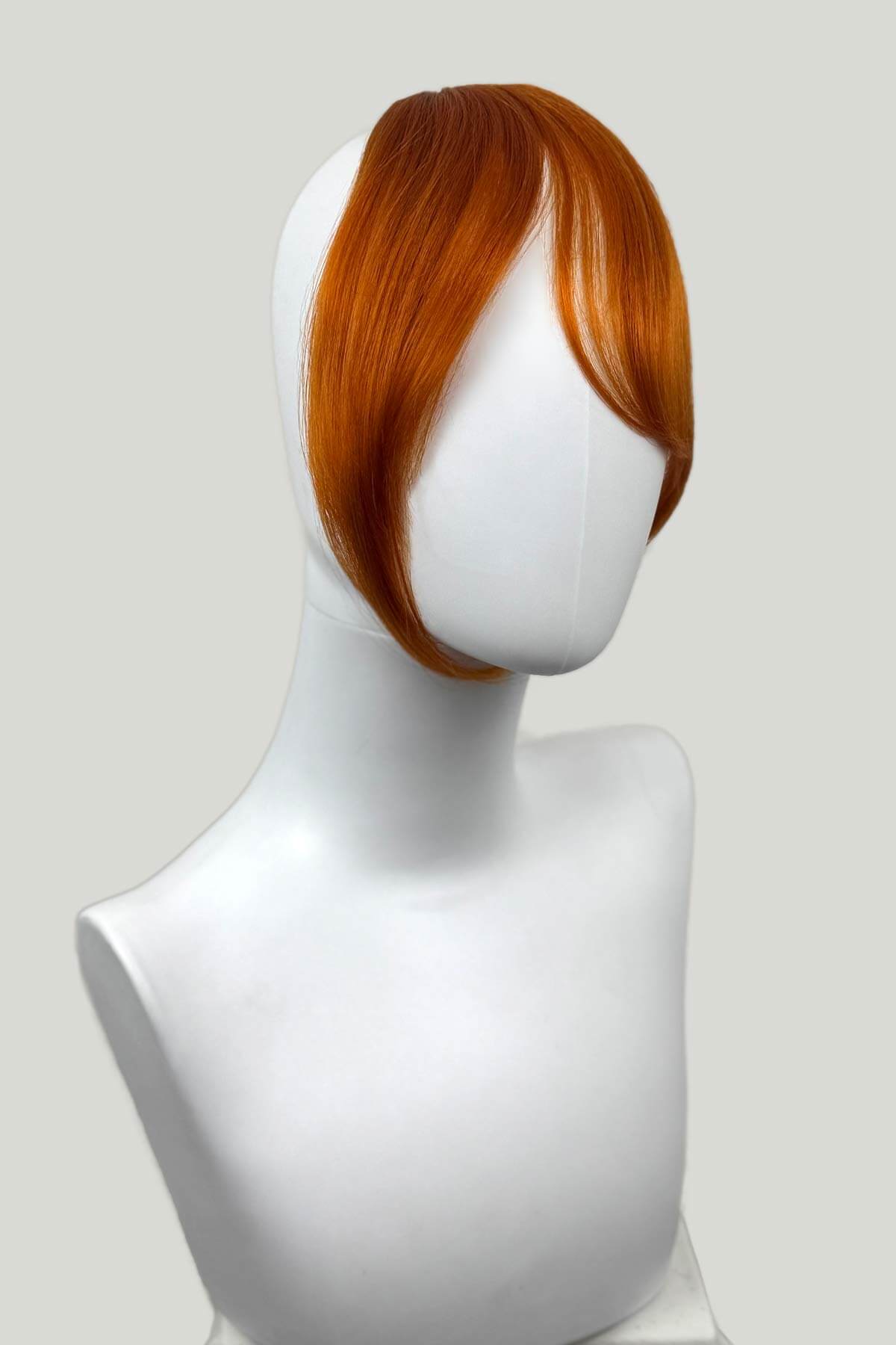 Mannequin head with a ginger hairpiece on a white background. Clip in fringe hairpiece/clip-in curtain bangs, with long, face framing wisps: Sabrina ginger