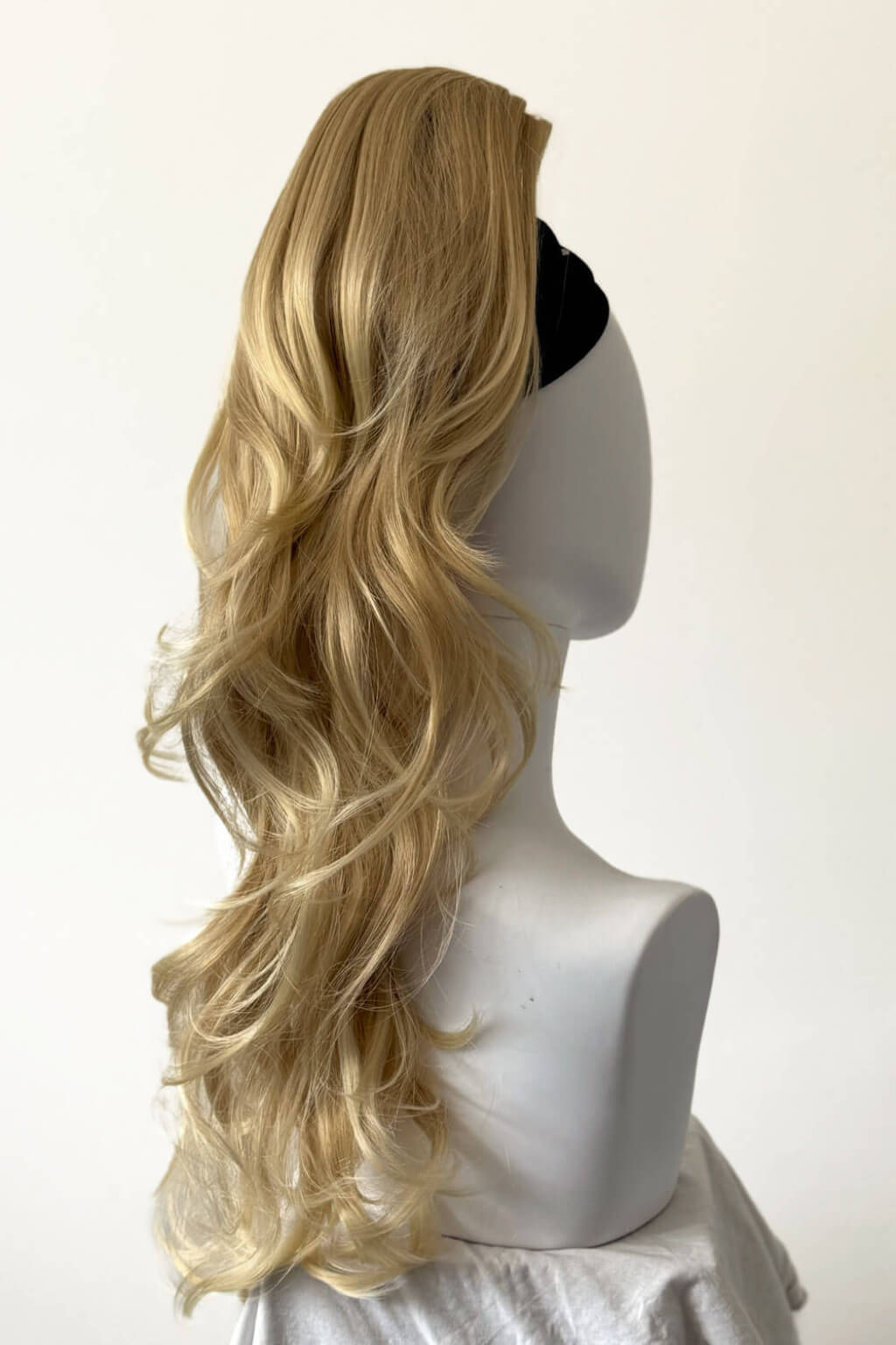Blonde wig on a mannequin head against a white background. Clip-in ponytail hairpiece extension: Olivia blonde 613T24