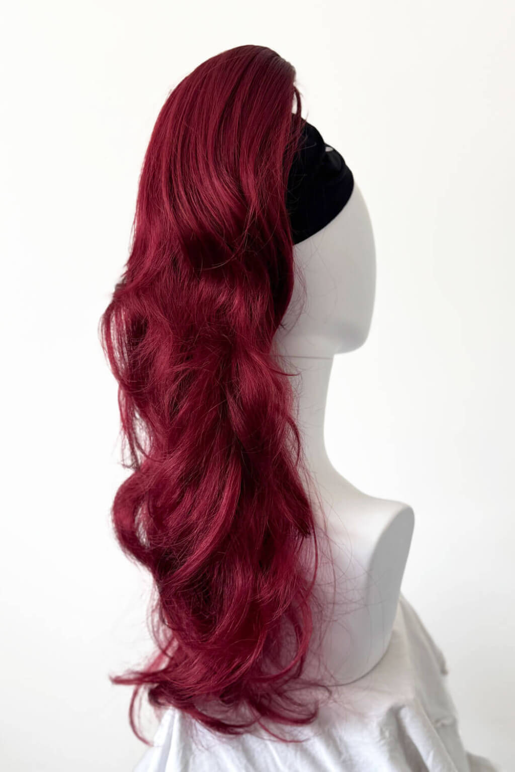 Red wig on a mannequin head against a white background. Clip-in ponytail hairpiece extension: Olivia Red 39