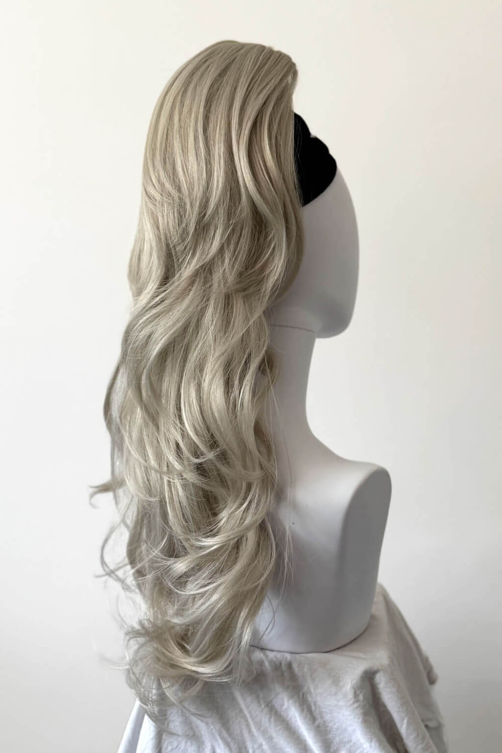 A long, wavy synthetic ponytail wig, displayed on a white mannequin head against a plain off-white background. Clip-in ponytail hairpiece extension: Olivia silver 60