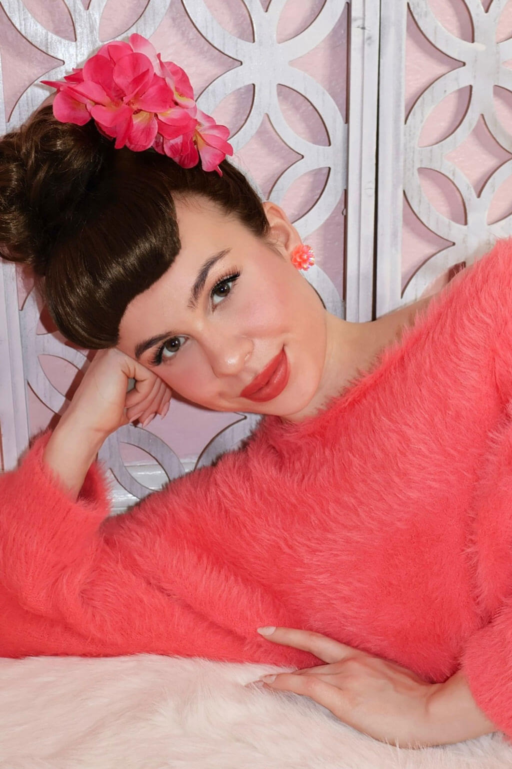 Woman in a pink robe with a decorative headpiece against a white lattice background