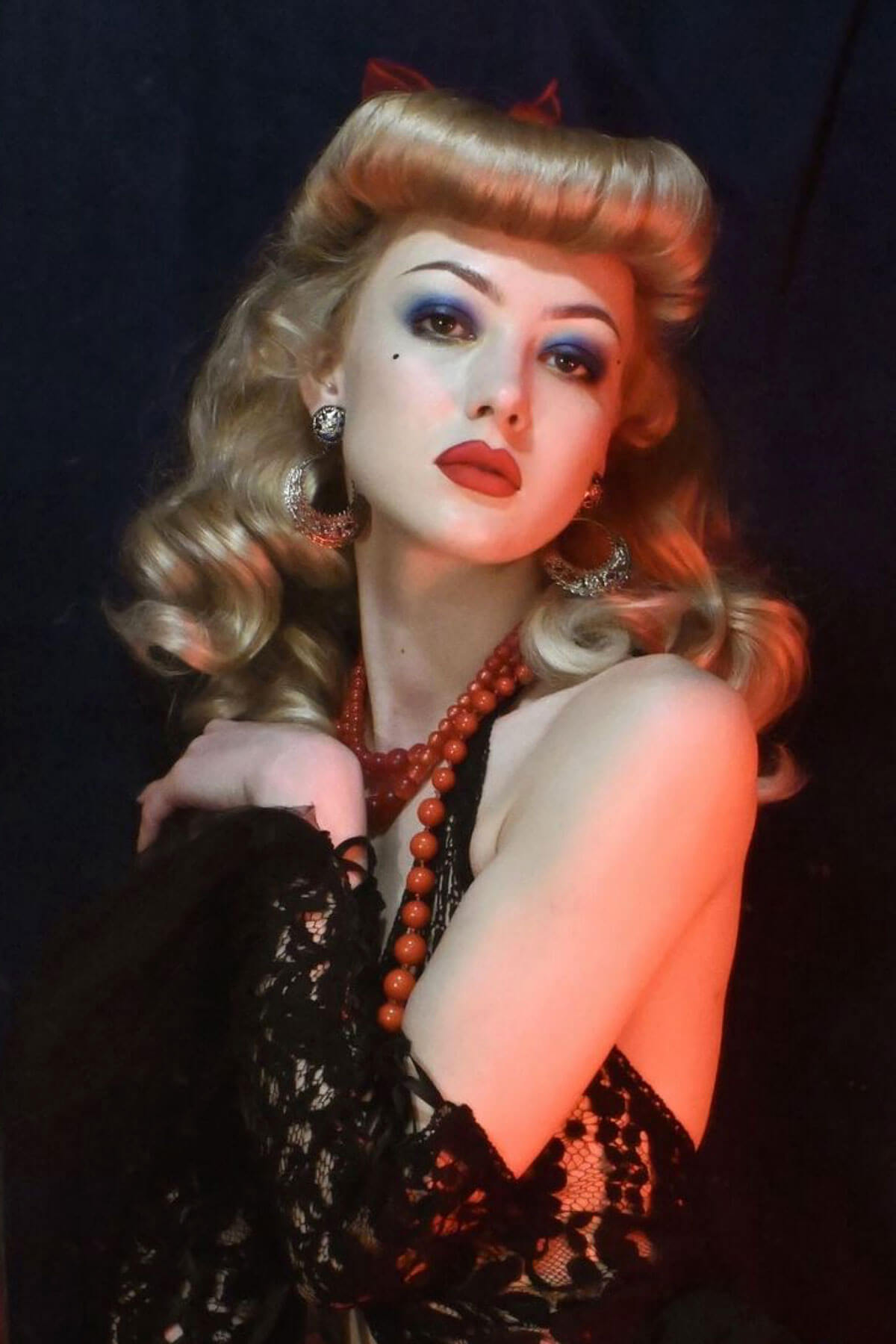 Person with vintage-style makeup and hair, wearing a black lace garment against a dark background. Bumper bangs pack - vintage 40s 50s fringe roll: Lena blonde 24H613