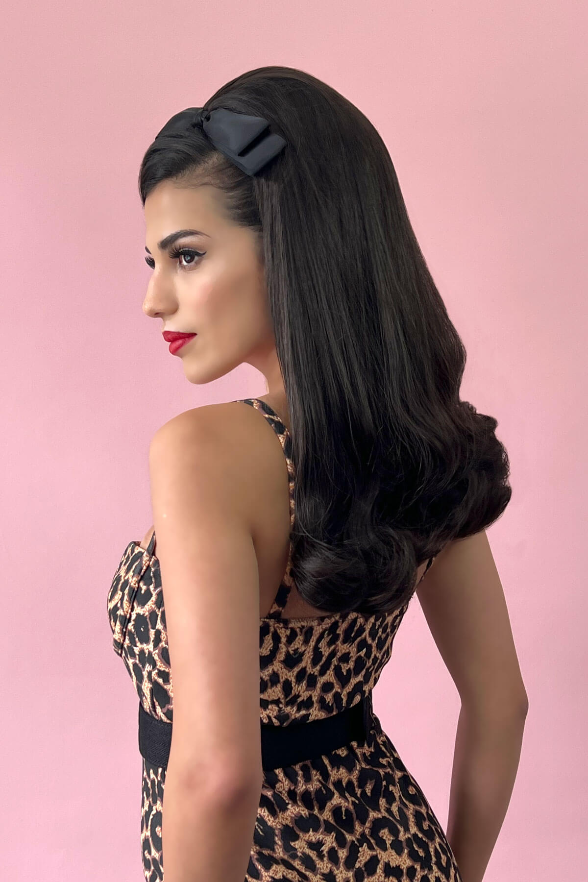 Woman with long, wavy hair wearing a black headband against a pink background. 1960s Retro high crown, half wig hairpiece, long with hair flip: Priscilla chestnut brown 8