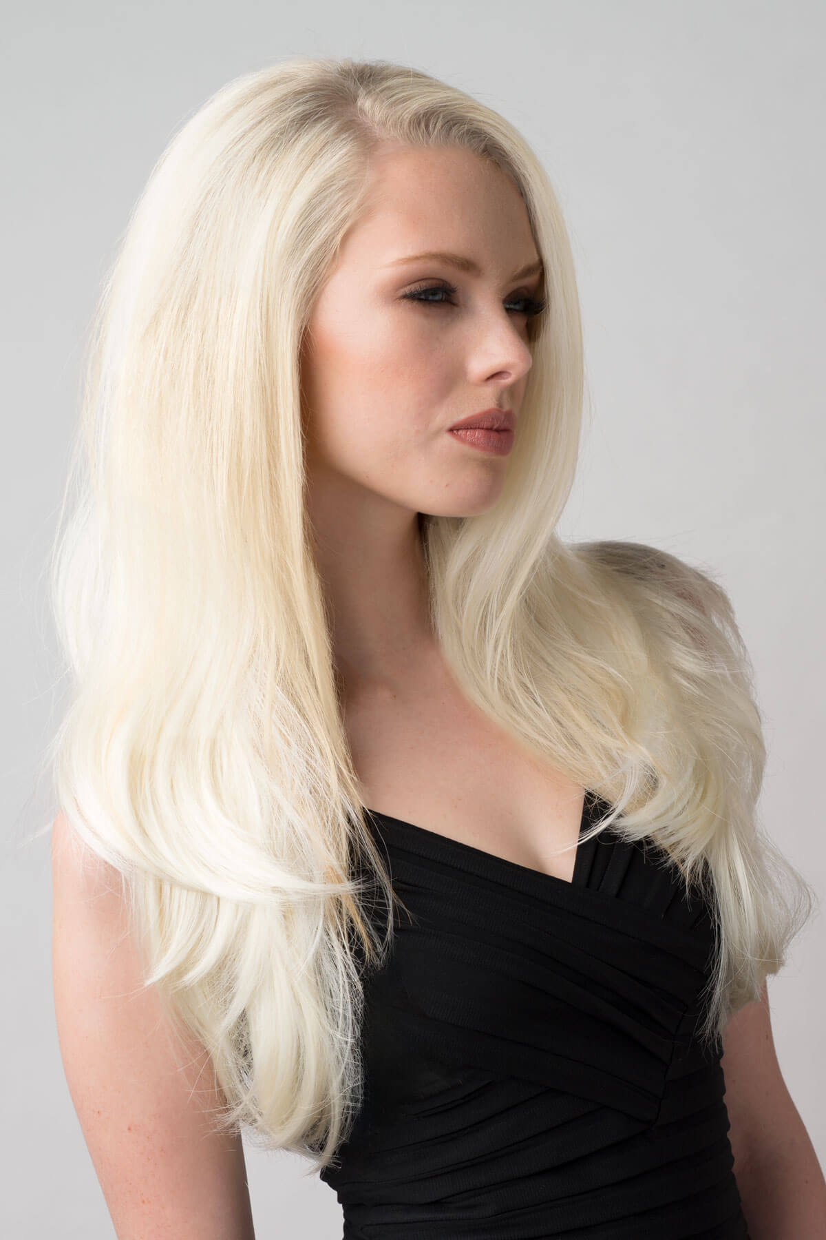 Woman with long blonde hair wearing a black dress against a gray background. Platinum blonde half wig hairpiece (3/4 wig), straight: Gwen