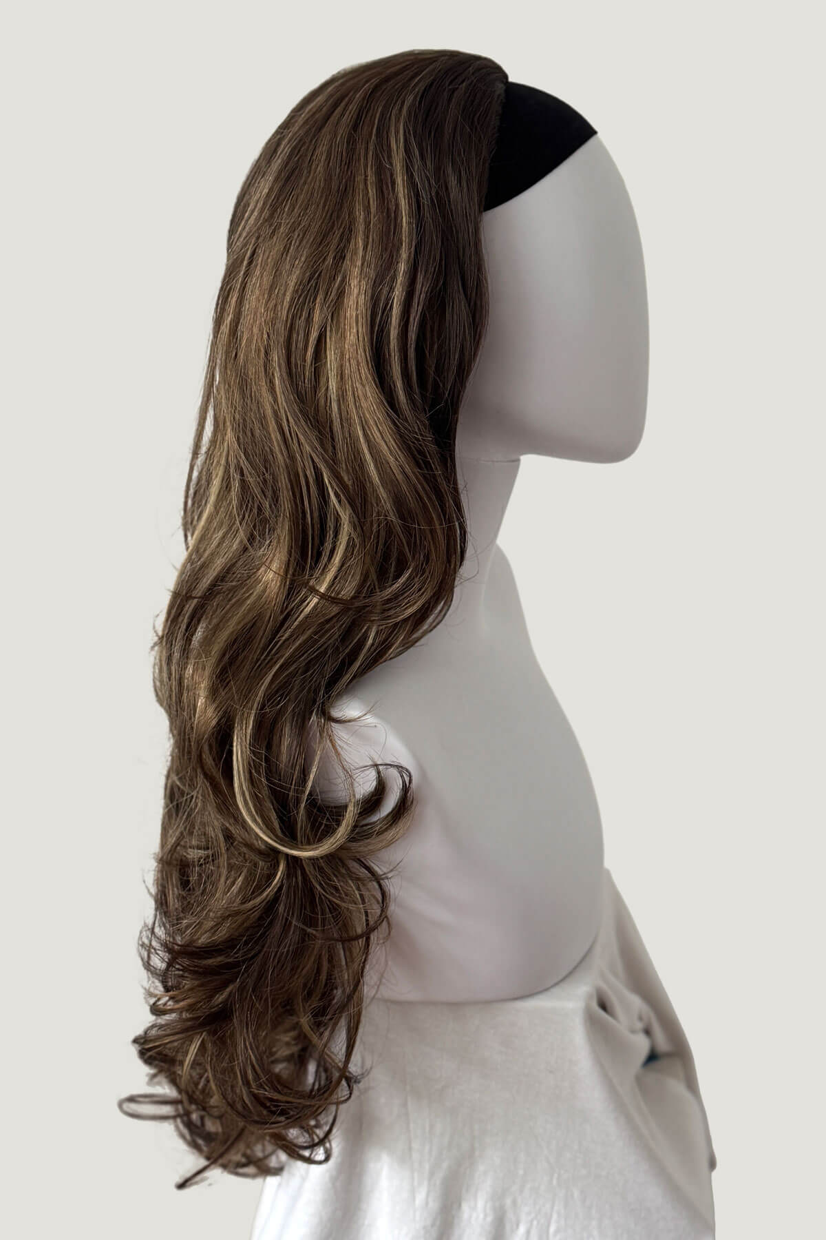 Long wavy brown hair extension on a mannequin head against a white background. Brown half wig with blonde highlights with big loose curls: Nickie