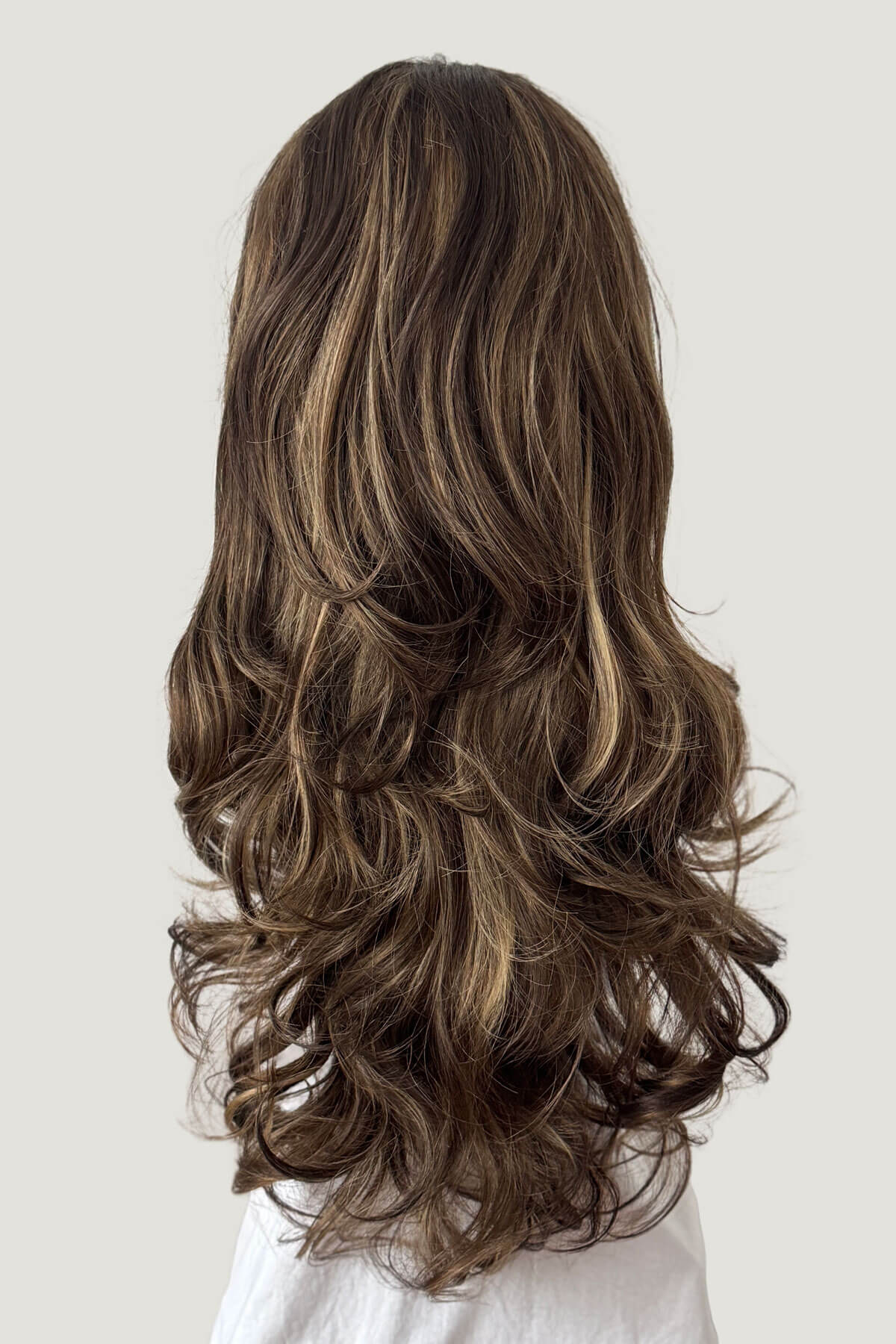 Long, wavy brown hair extension on a plain background. Brown half wig with blonde highlights with big loose curls: Nickie