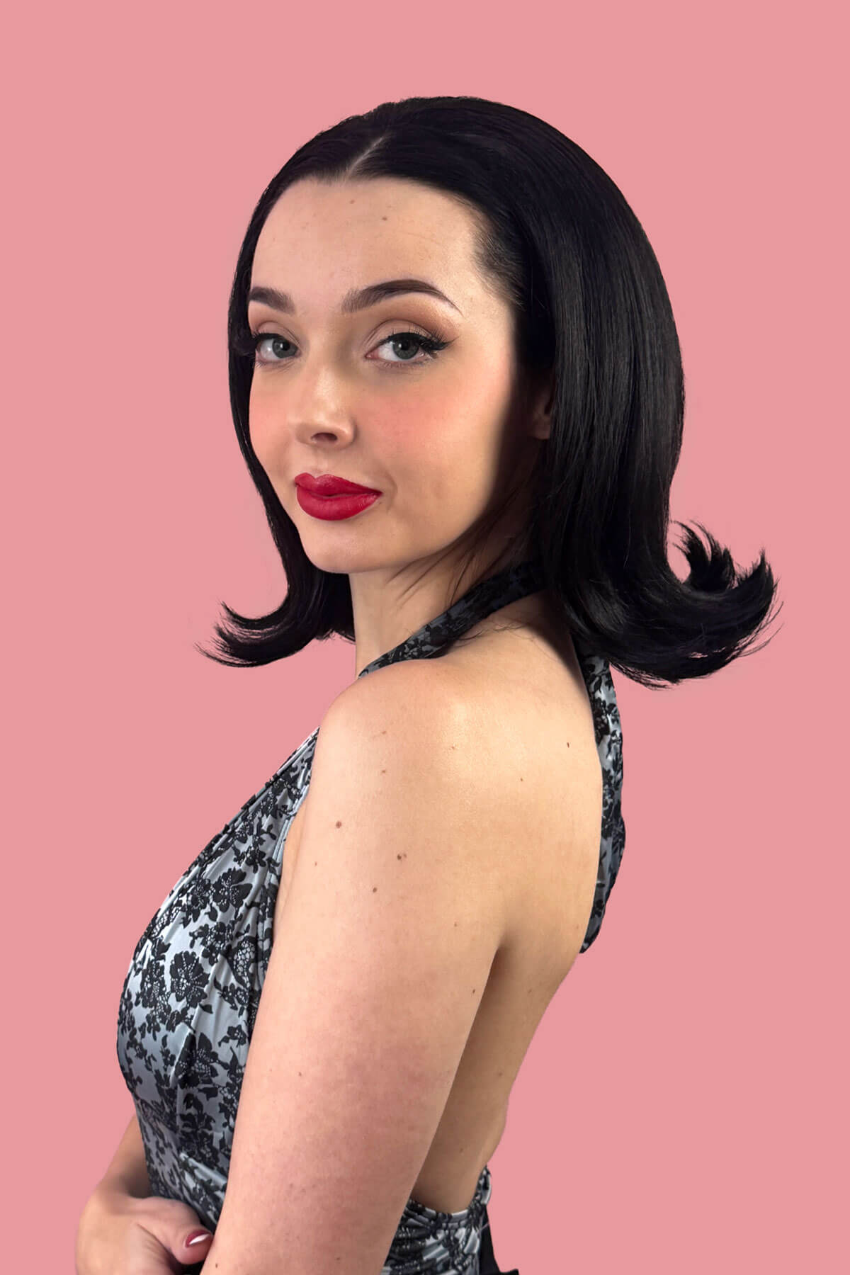 Woman with styled hair and red lipstick against a pink background. Short, flipped bob half wig: Samantha Black 1B