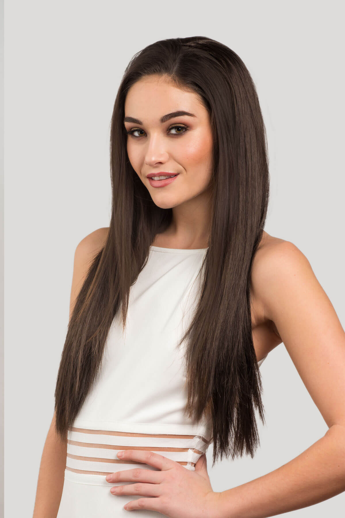 Woman with long brown hair wearing a white dress on a light gray background. Straight brown half wig hairpiece extension, long: Faye dark brown 6
