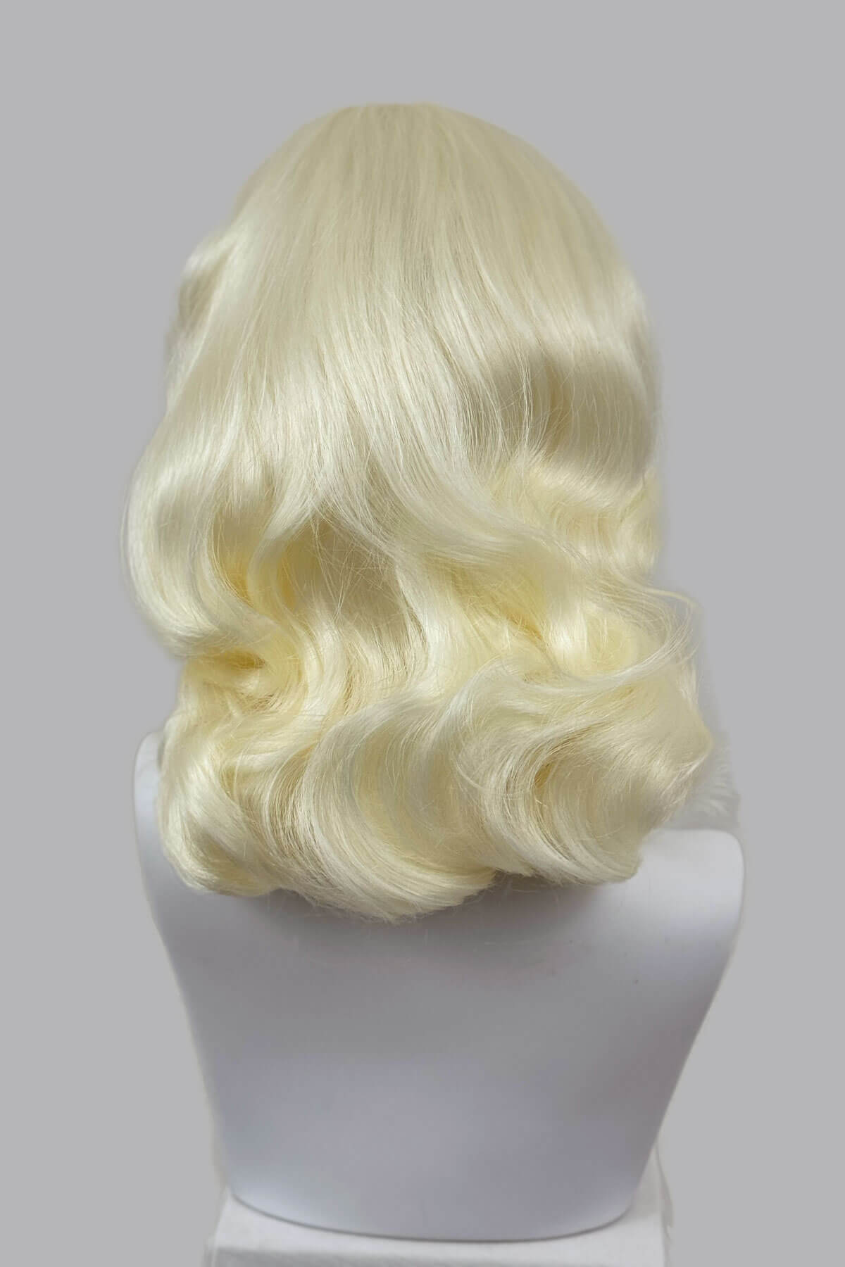 Blonde wig on a mannequin head against a grey background viewed from the back. 1950s style shoulder length half wig hairpiece with beautiful vintage waves: Onyx platinum blonde 1001