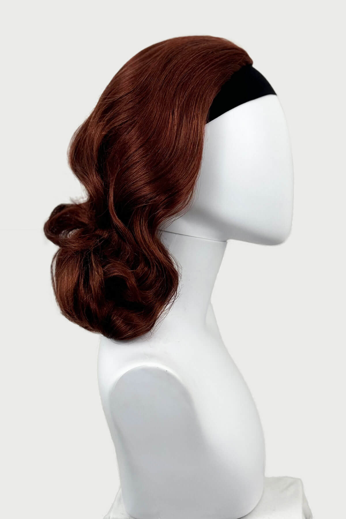 Brown wig on a white mannequin head against a white background, viewed from the side. 1950s style shoulder length half wig hairpiece with beautiful vintage waves: Onyx copper red 130