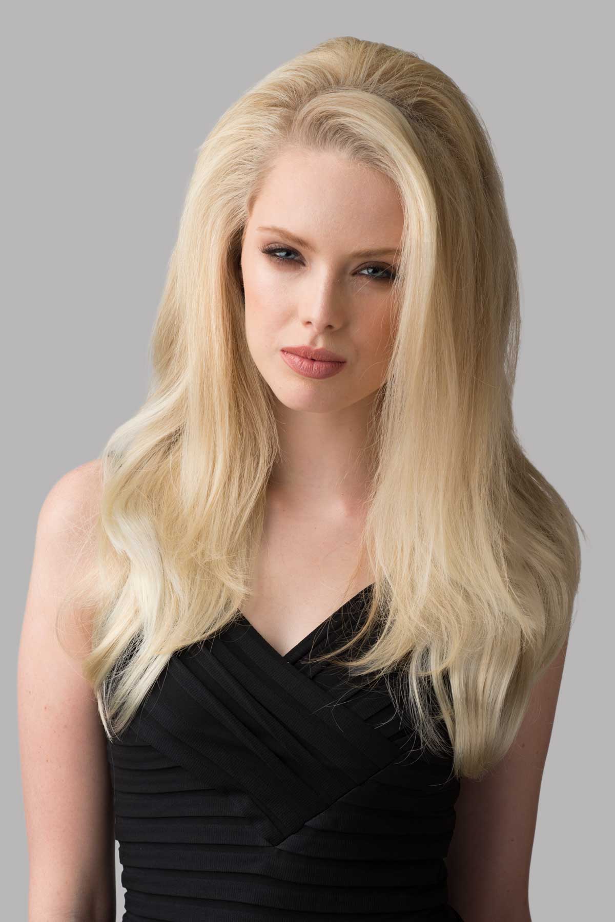 Woman with long blonde hair wearing a black dress against a gray background. Straight half wig with high crown; height boosting technology: Claudia