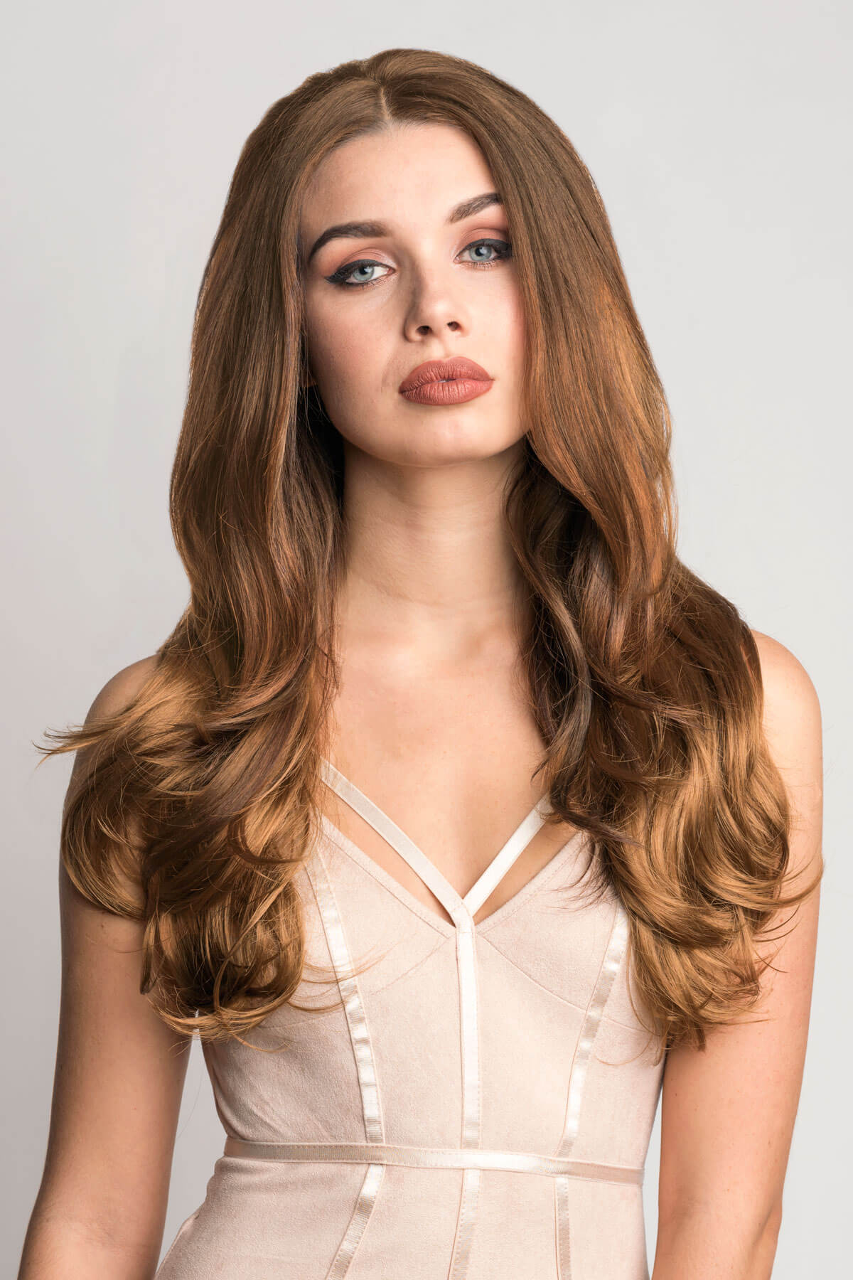 Woman with long, wavy brown hair wearing a beige dress against a light background. Brown half wig hairpiece (3/4 wig), layered, wavy: Simone auburn 27