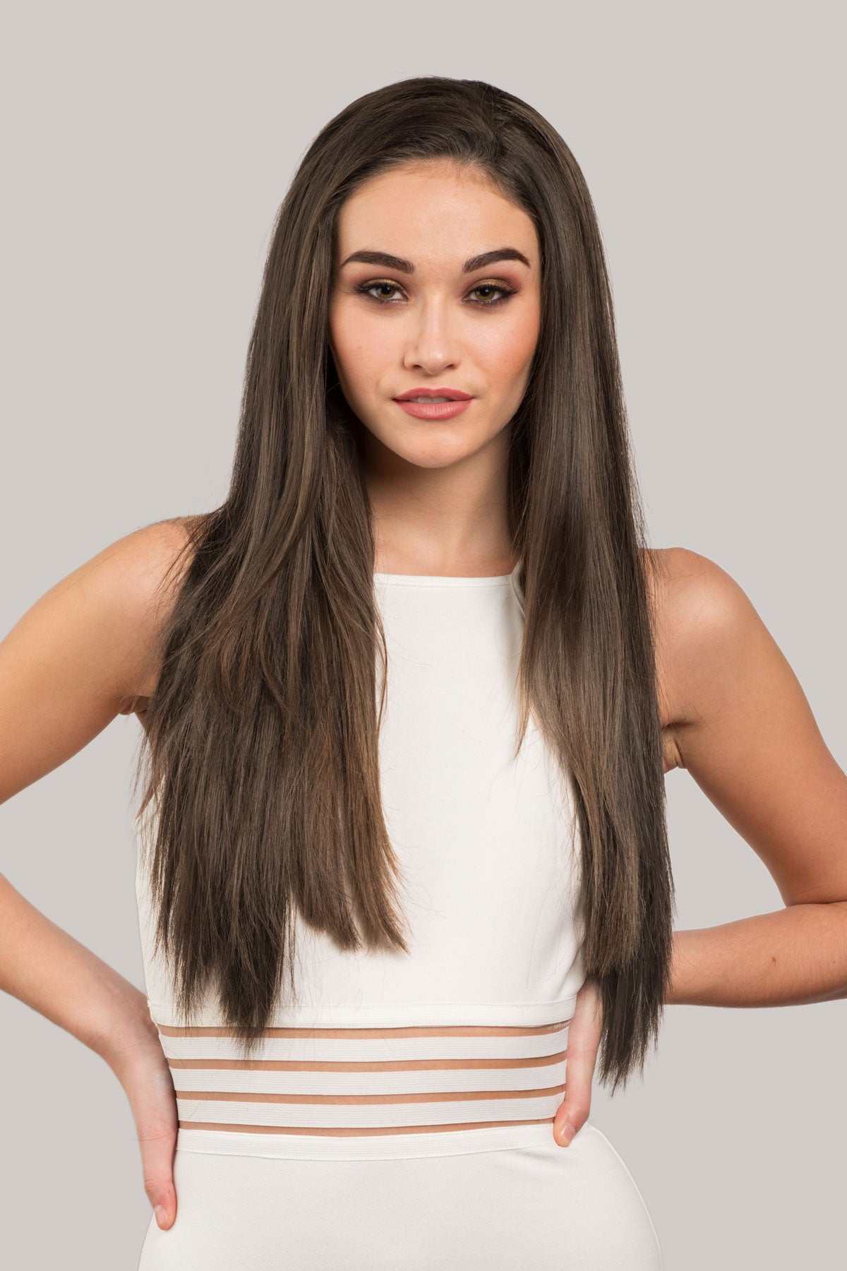 Woman with long brown hair wearing a white top against a gray background. Straight brown half wig hairpiece extension, long: Faye Mocha brown 10
