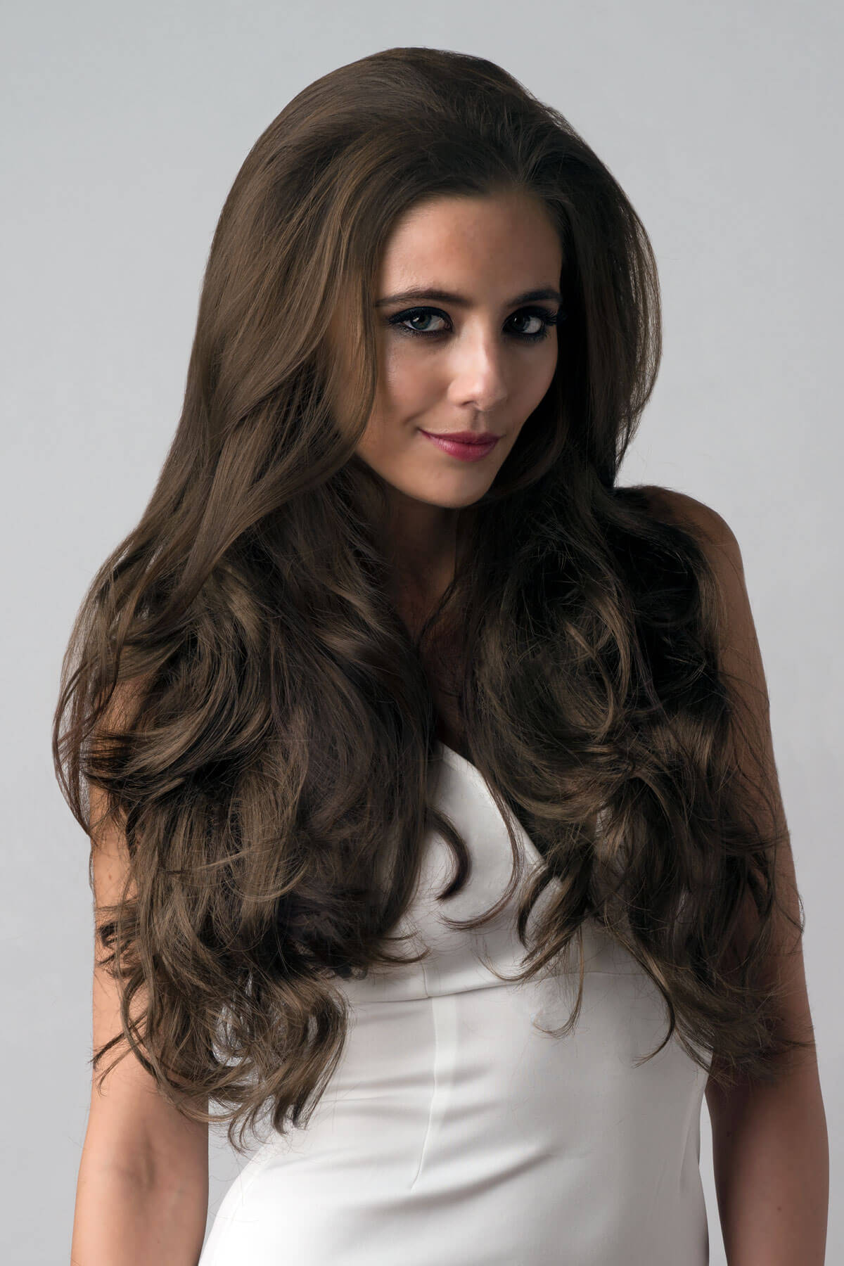 Woman with long, wavy brown hair wearing a white top against a gray background. Brown half wig hairpiece, full, long with gentle waves: Taya mocha brown 10