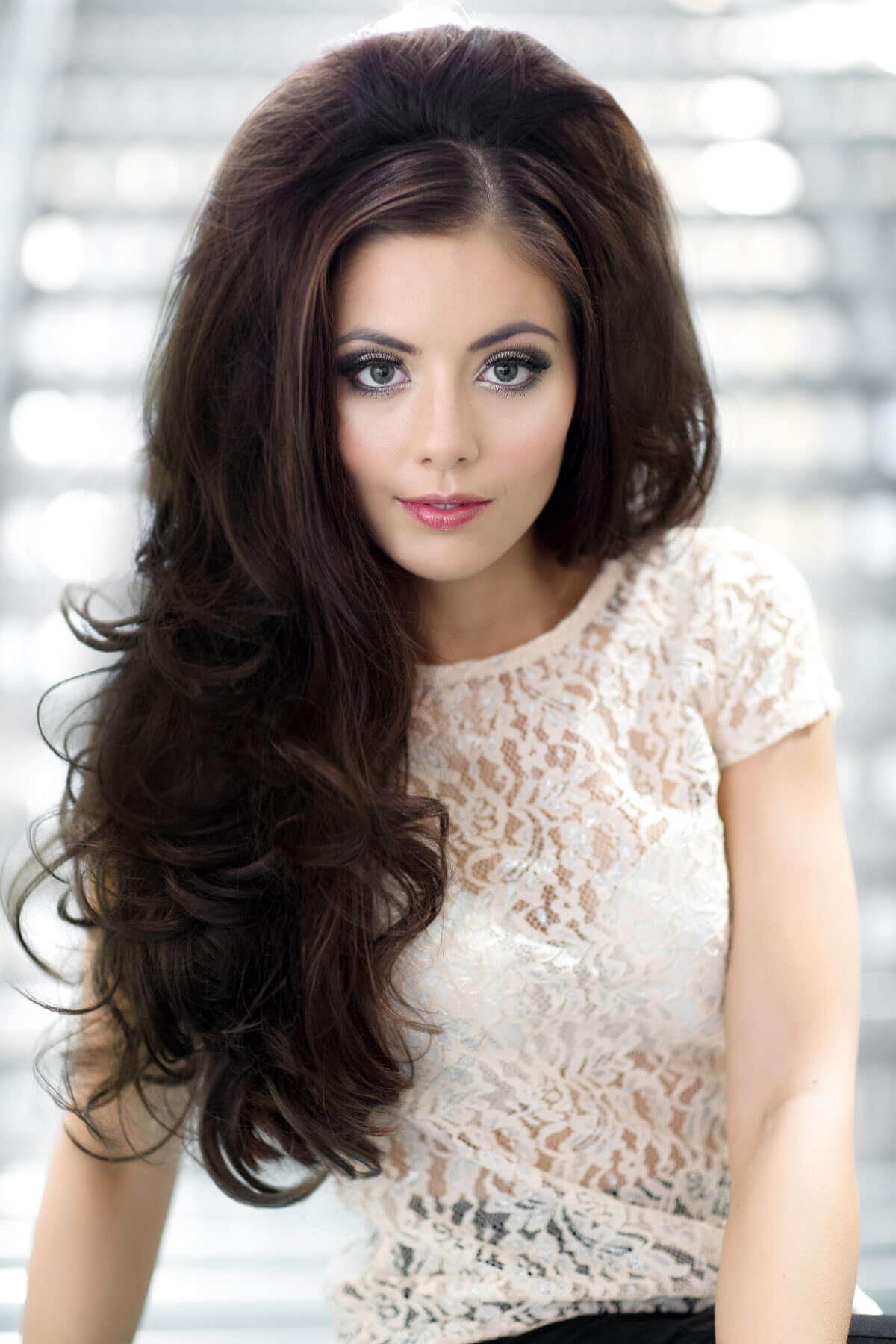 Woman with long, wavy hair wearing a white lace top against a blurred background. Volume boosting 3/4 hairpiece, long, wavy, heat styeable: Gisele chestnut brown 8