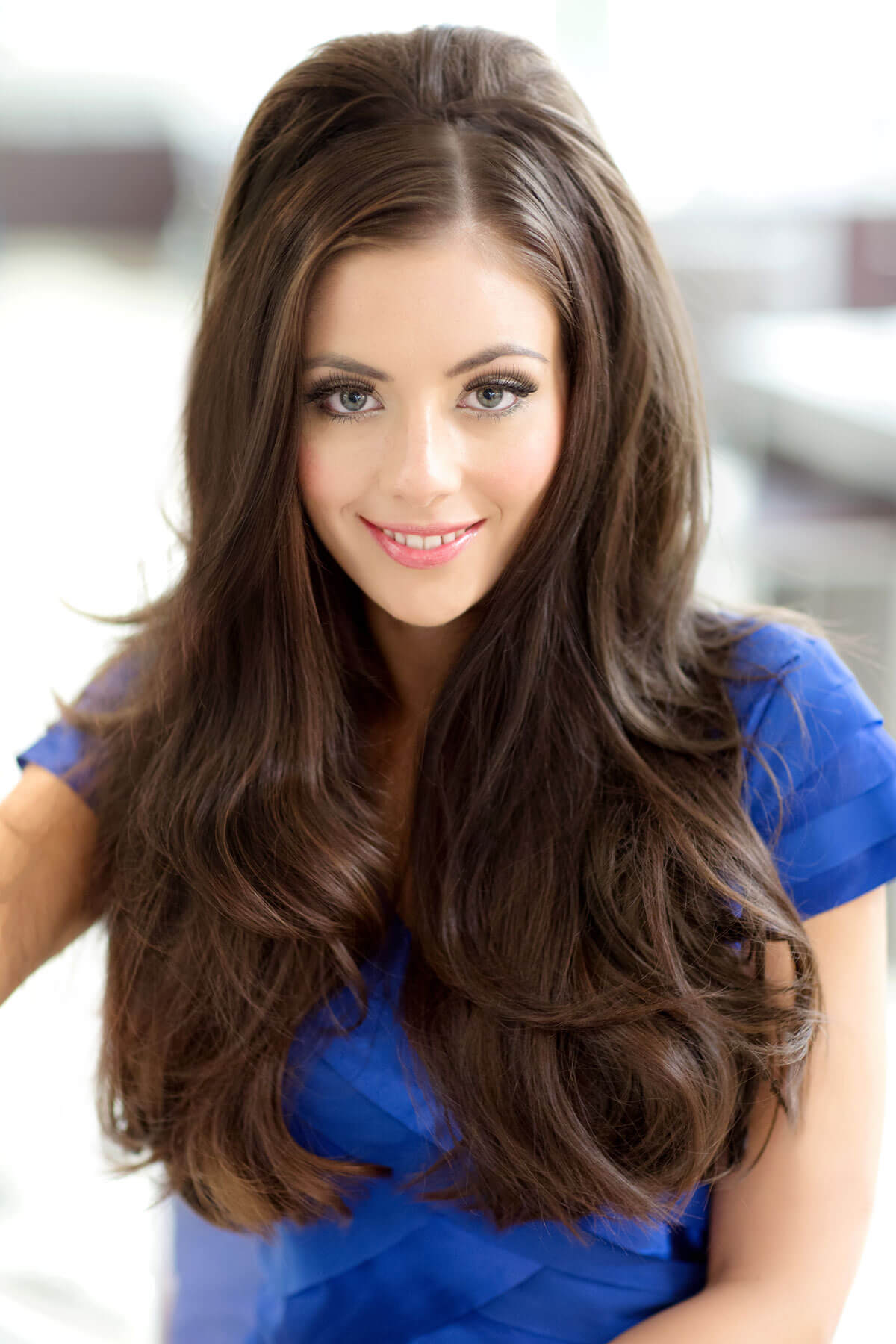 Woman with long brown hair wearing a blue dress against a blurred indoor background. Volume boosting 3/4 hairpiece, long, wavy, heat styeable: Gisele chestnut brown 8