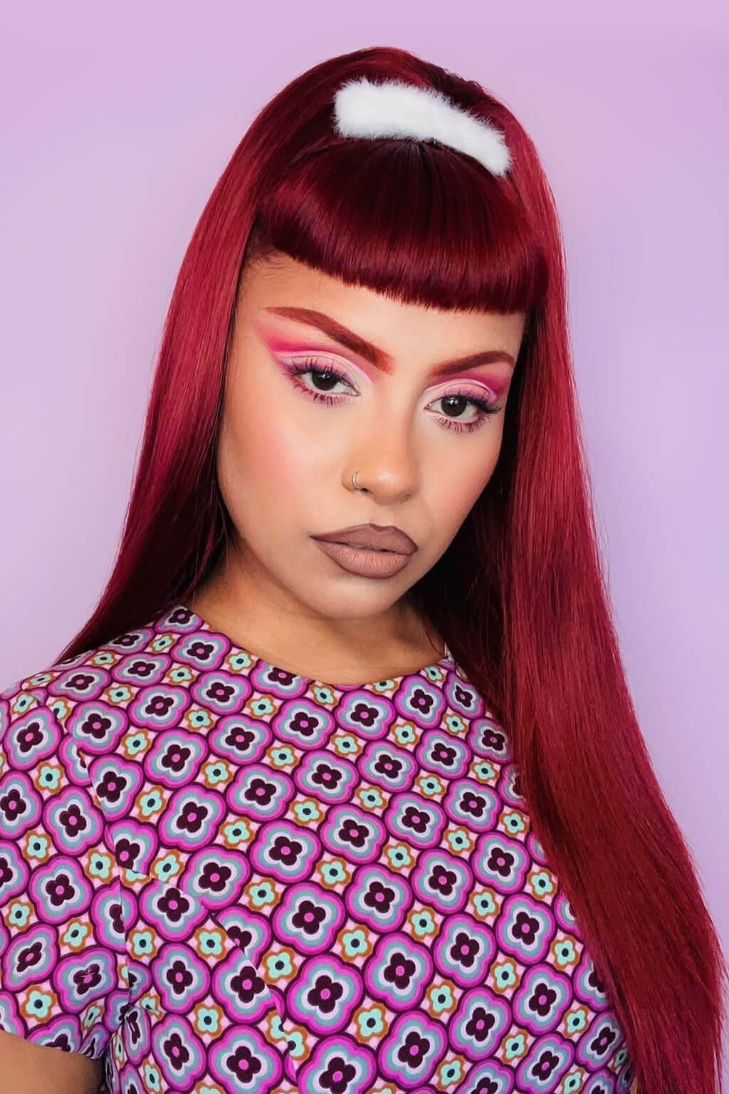 Person with long red hair and colorful makeup against a light purple background. 1960s style hair, high crown long straight half wig: Andrea cherry red 39