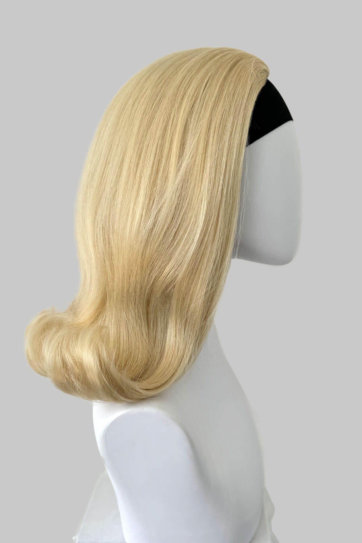 Blonde wig on a mannequin head against a gray background. 1960s half wig hairpiece, flicked, hair flip: Philippa blonde 613