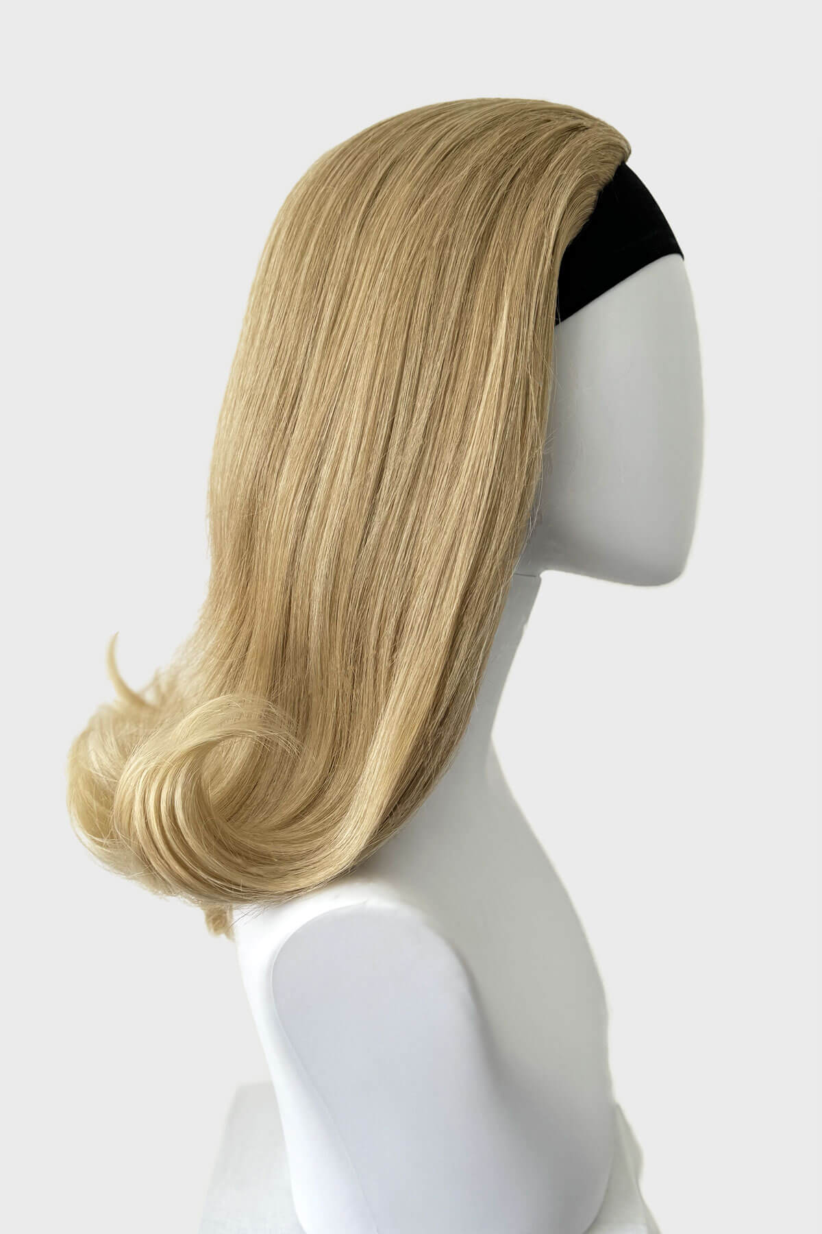 Blonde wig on a mannequin head against a white background. 1960s half wig hairpiece, flicked, hair flip: Philippa blonde 613T24