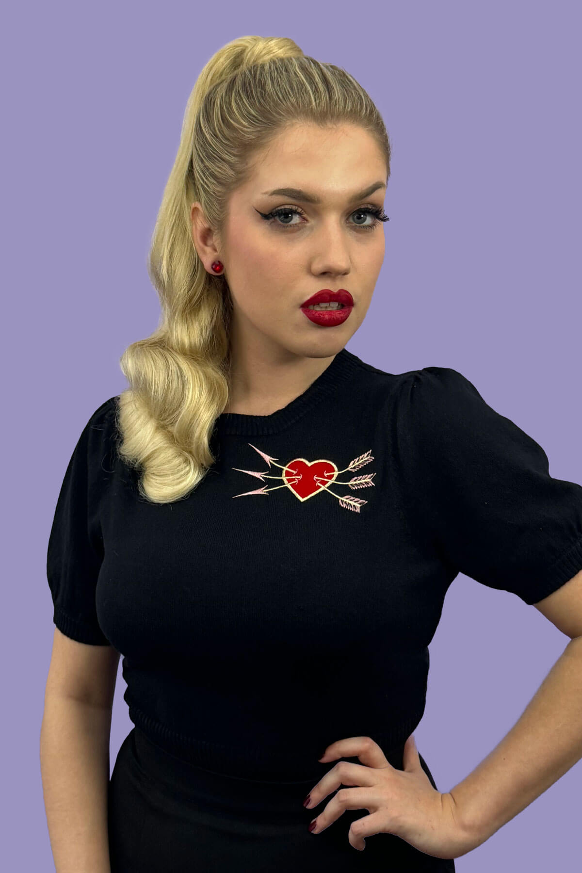 Woman wearing a black t-shirt with a heart and arrow design on a purple background. Retro style ponytail hairpiece, long with vintage waves: Arabella