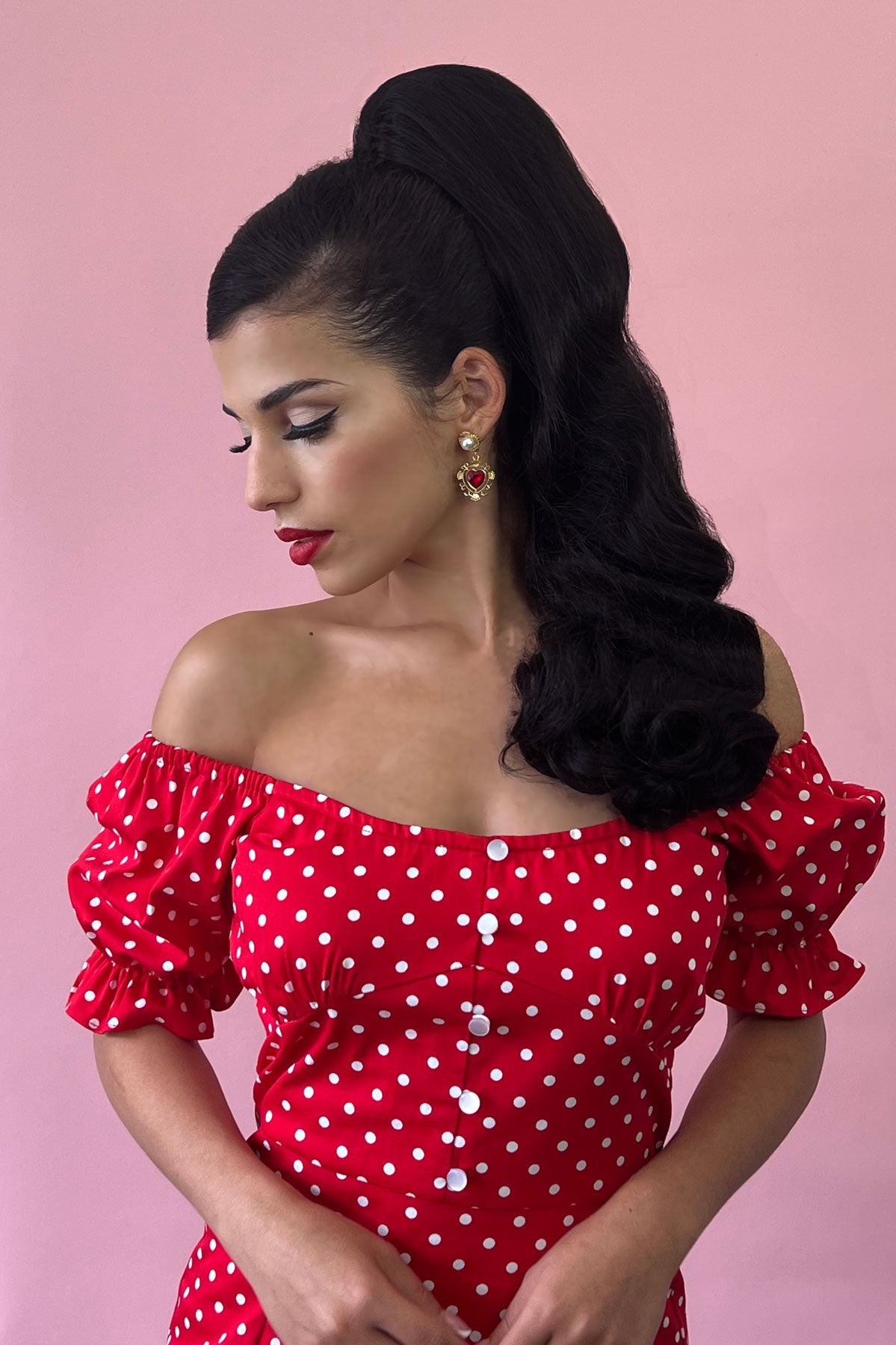 Woman wearing a red polka dot dress with puffed sleeves against a pink background wearing a retro style ponytail hairpiece, long with vintage waves: Arabella black 1B