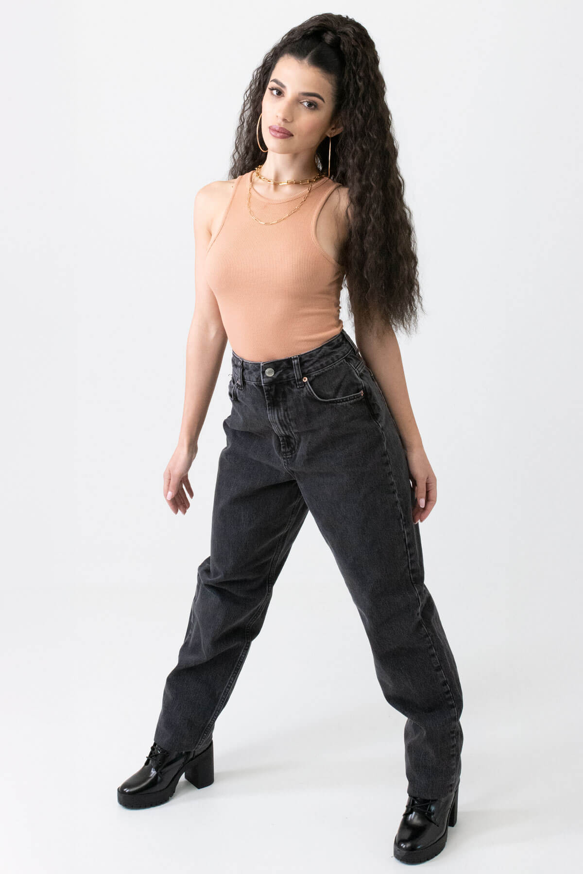 Woman wearing black jeans and a beige top on a white background. Extra long ponytail extension with long loose spirals: Kaia dark brown 4