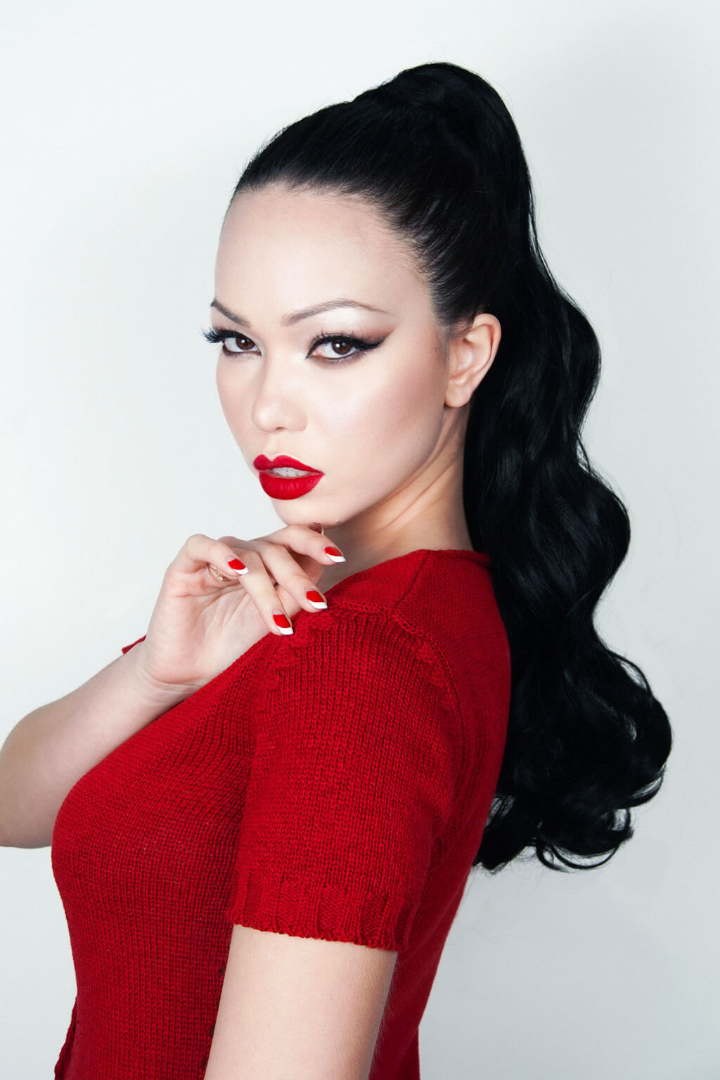Woman with long black hair styled in a high ponytail, wearing a red top against a white background. Long ponytail hairpiece with vintage waves: Kitrysha - Jet Black 1