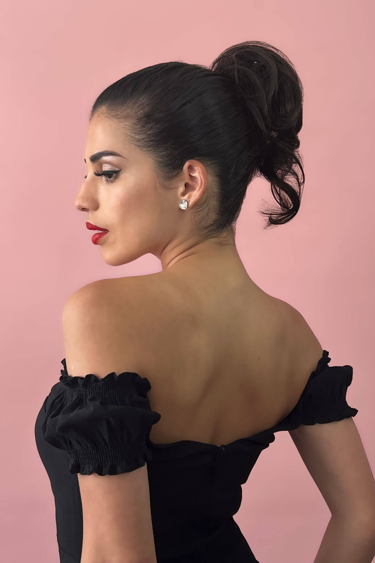Woman in a black off-shoulder dress with red lipstick against a pink background. Short ponytail extension hairpiece, short with whisps: Leah ginger