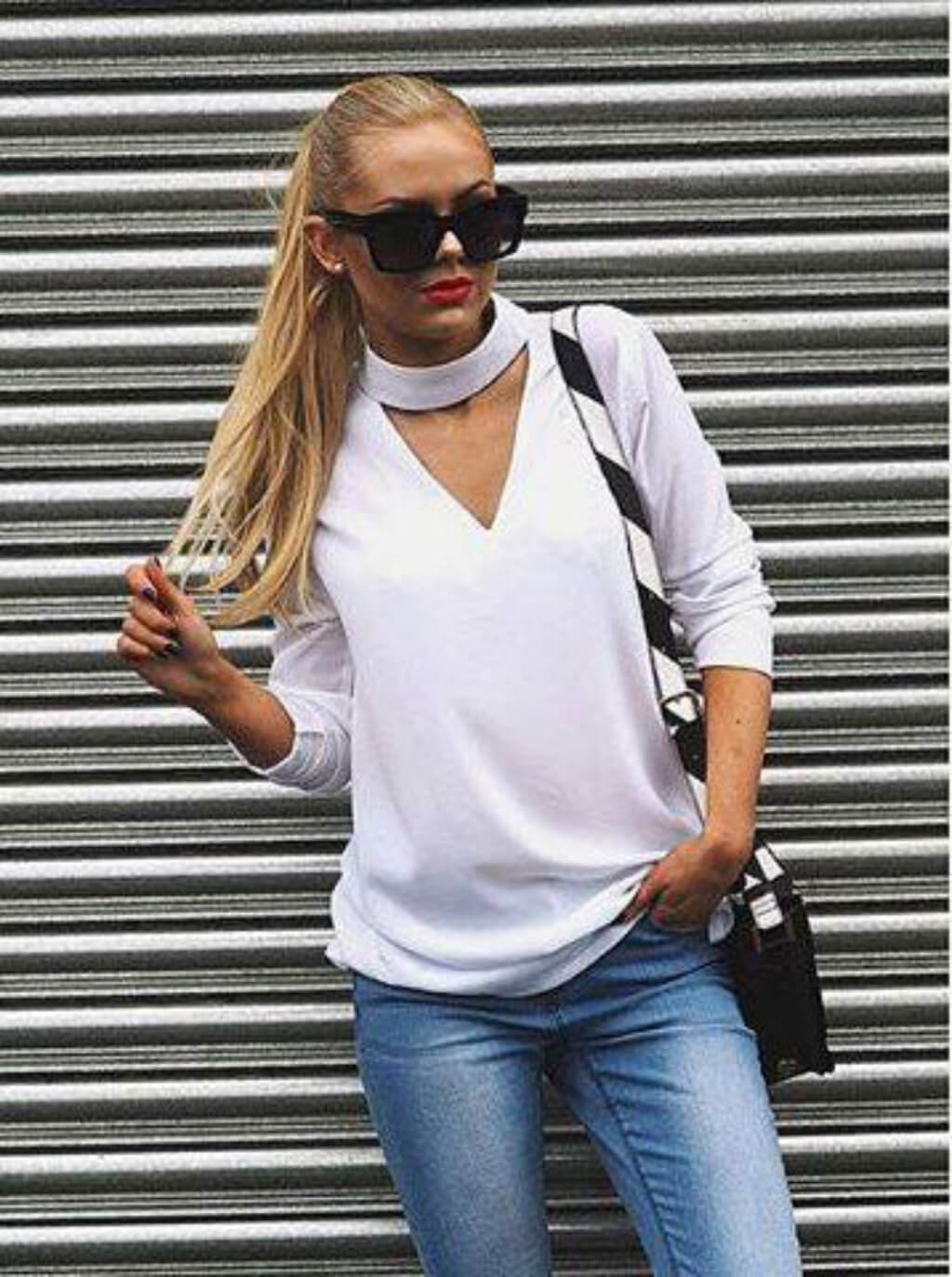 Woman wearing a white long-sleeve top and blue jeans against a metallic background. synthetic hair piece Long ponytail extension with gentle, sleek, layered waves: Mali blonde 24BH613