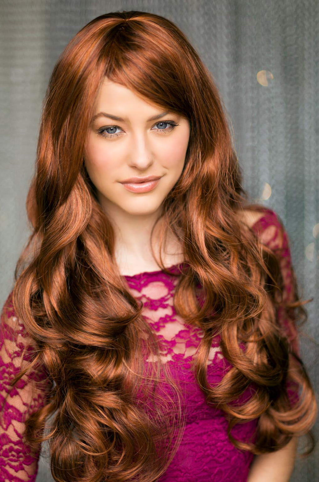 A person wearing a red and auburn wig with blonde highlights, featuring long bouncing curls and waves with a side sweeping fringe. Red & auburn wig with blonde highlights, long: Freya