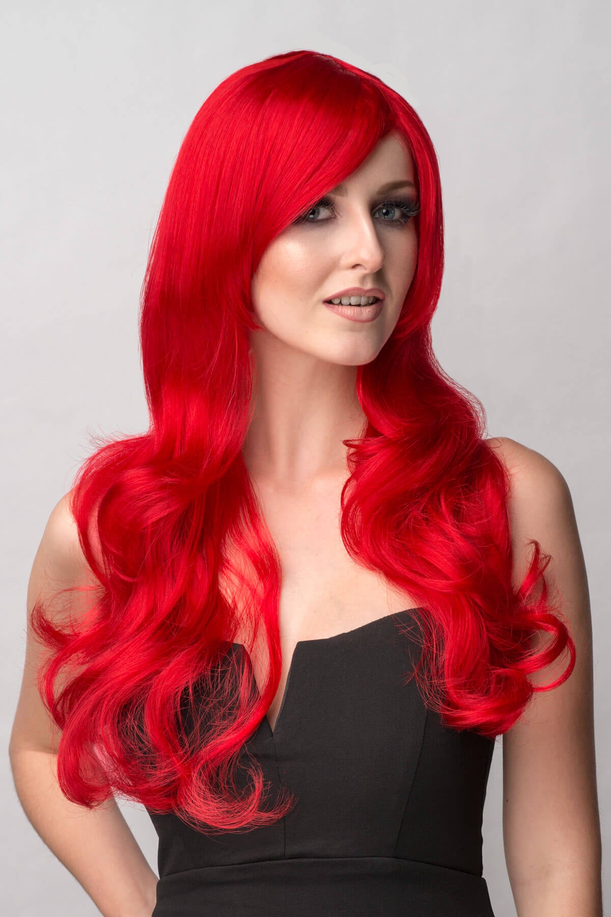 Woman with vibrant red hair wearing a black top against a gray background. Long bright red wig with long, big loose curls: Alexis