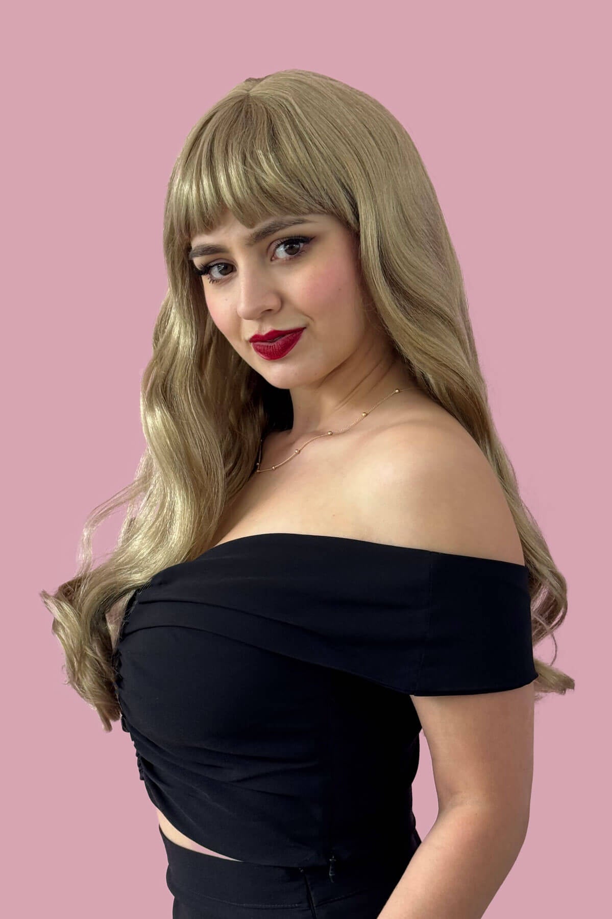 Woman with blonde hair and red lipstick wearing a black off-shoulder top against a pink background. Long blonde wavy wig with pinup-style fringe: Elena