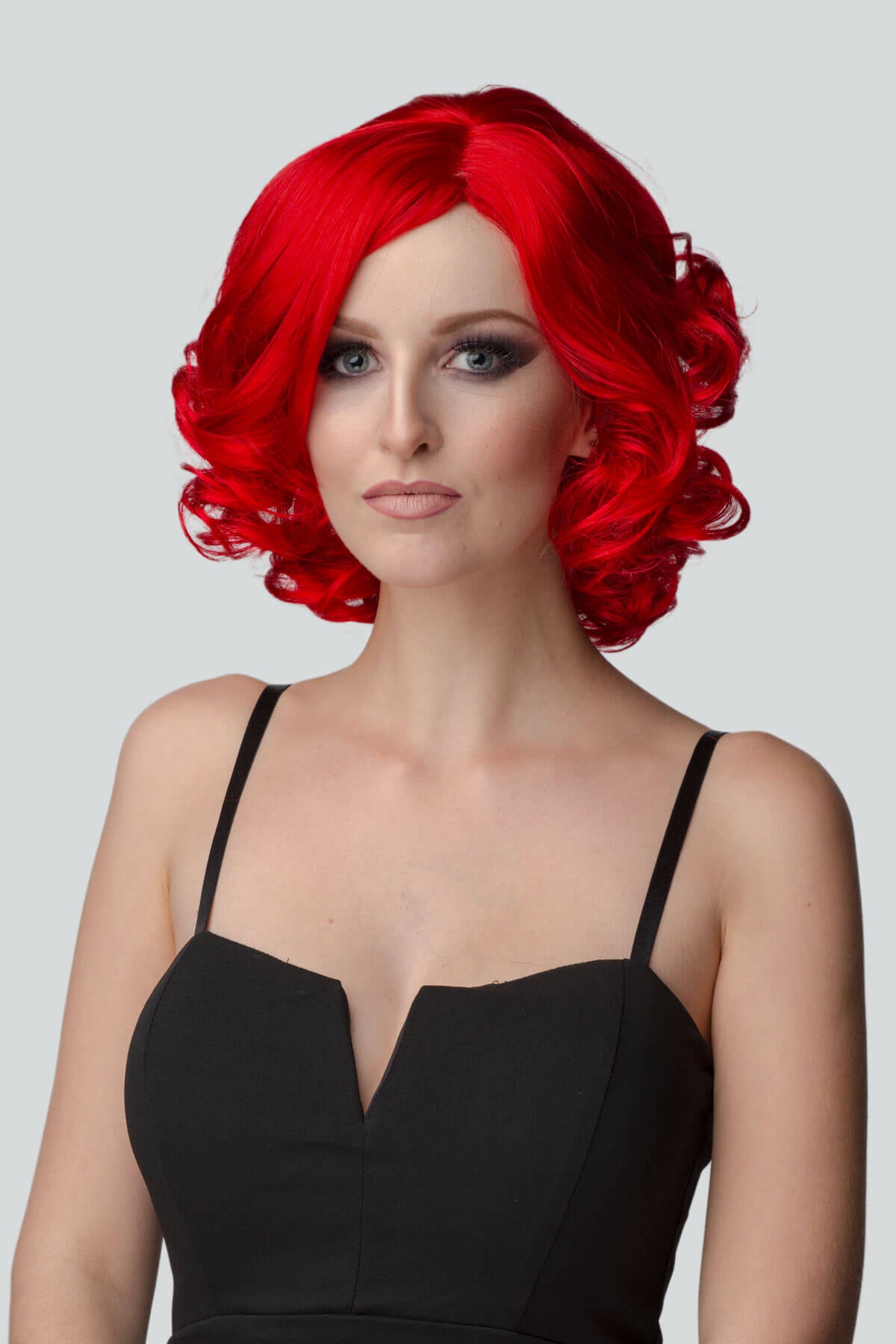 Woman with red wig and black dress on gray background. Rihanna style red wig, short with curls: Rihanna