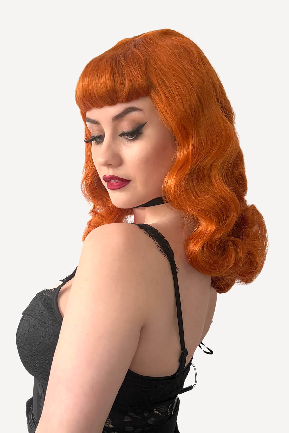 Woman with ginger red hair styled in vintage fashion against a white background. Ginger pinup style wig, finger waved with short fringe: Sienna