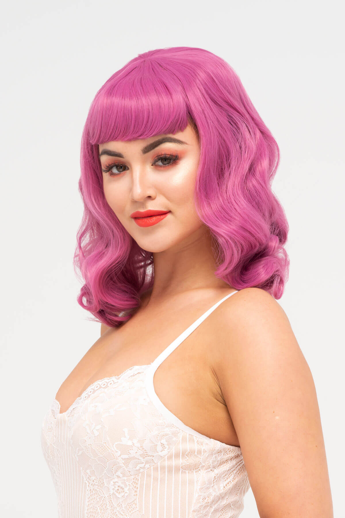 Woman with pink wig and red lipstick against a white background. Pink pinup style wig, with finger waves and a short fringe, 1950s style: Stevie dark pink 2520J