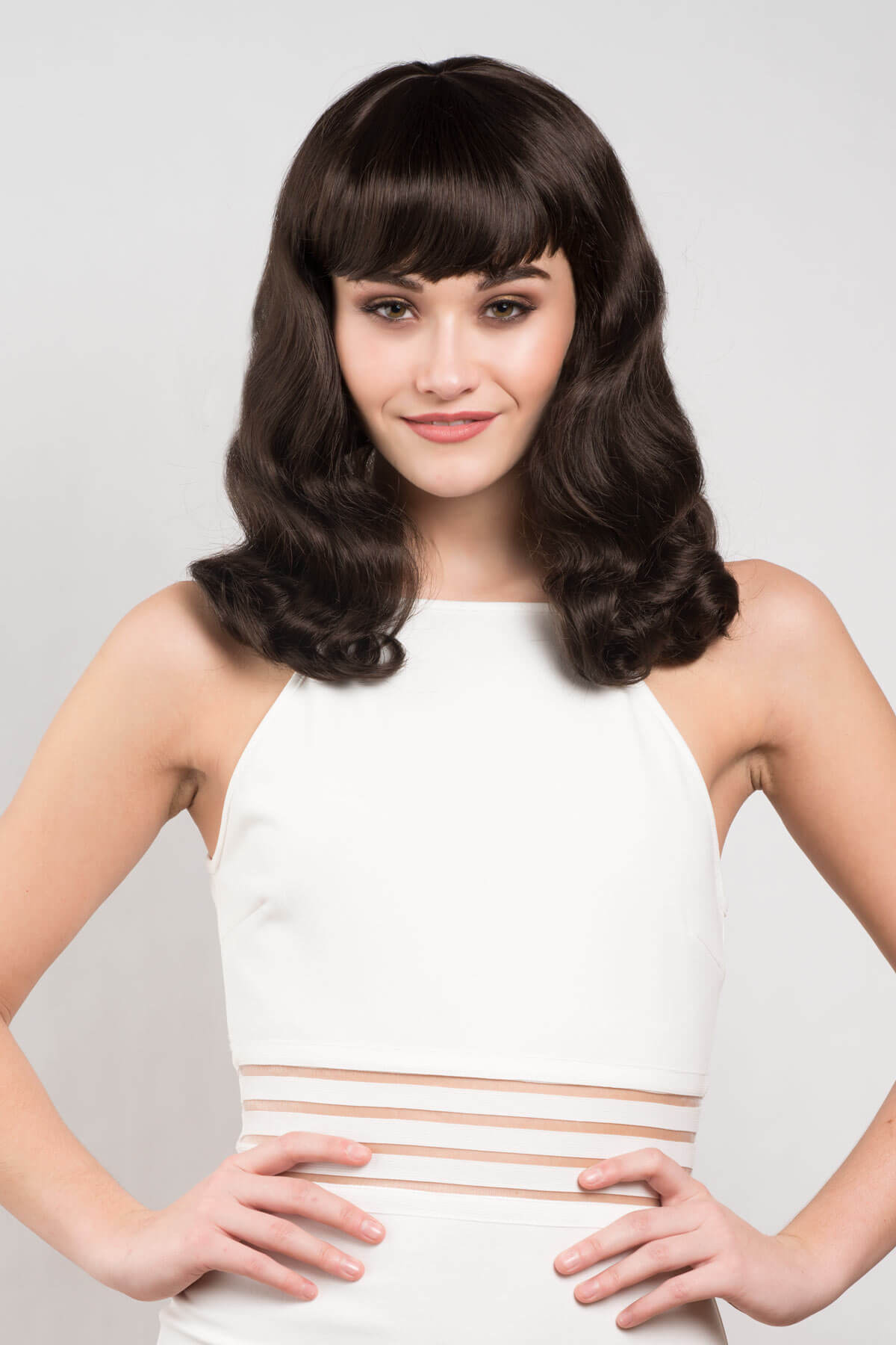 Woman with styled hair wearing a white dress against a plain background. Dark brown pinup style wig, finger waved with short fringe, 1950s style: Becca