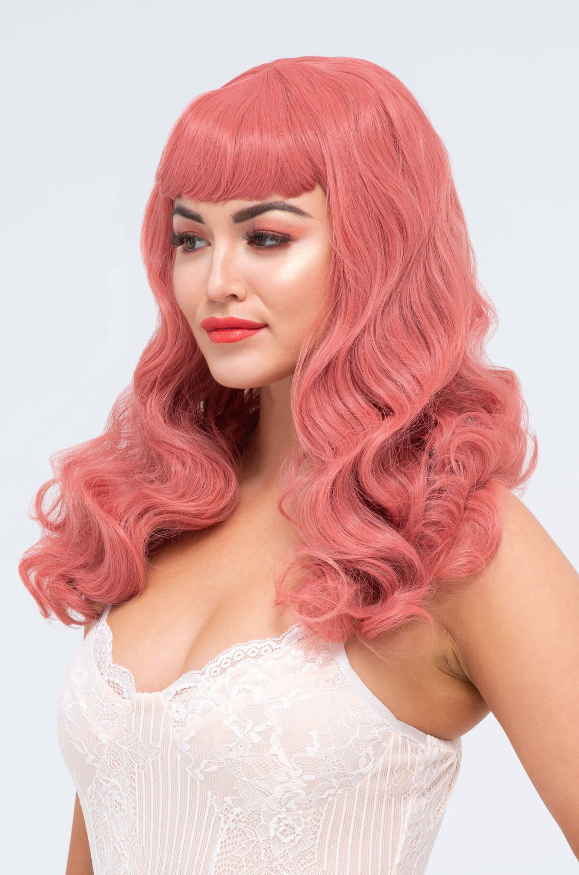 Woman with pink wig and white dress on a light gray background. Long pastel-pink pinup style wig with gentle waves and short fringe: Candy