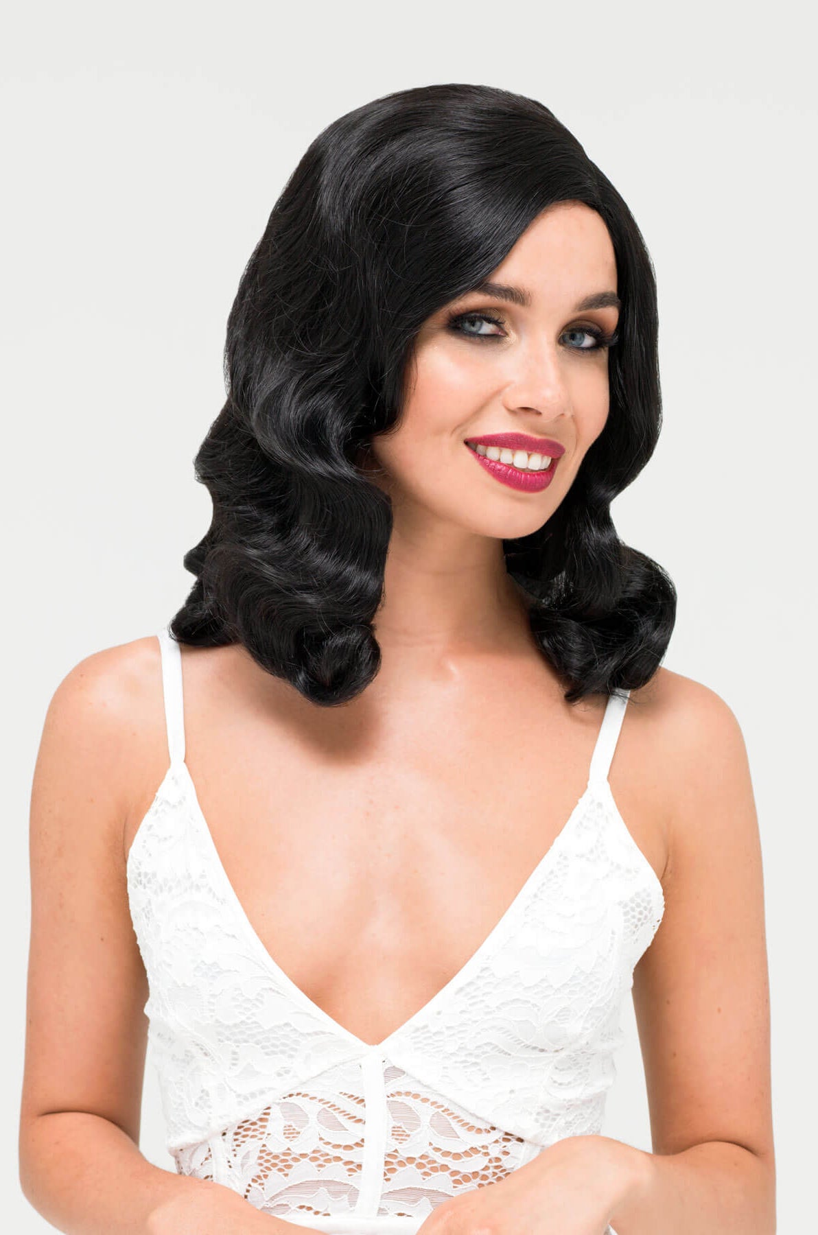 Woman with styled black hair wearing a white lace top on a light gray.background. Black 1940s style wig with long marcel waves: Vivienne