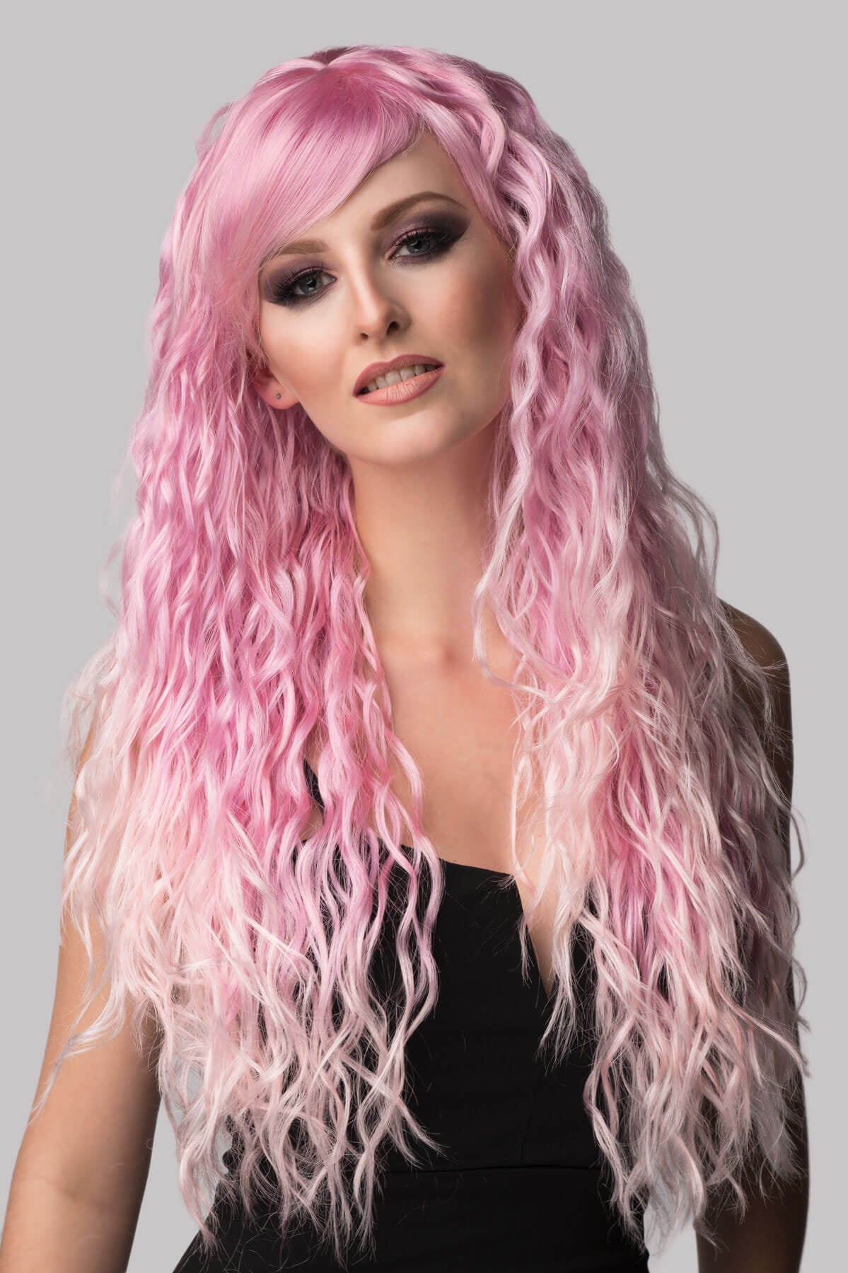 Woman with long pink wig on a gray background. Crimped pink wig, long, in two colour pink ombre: Peony