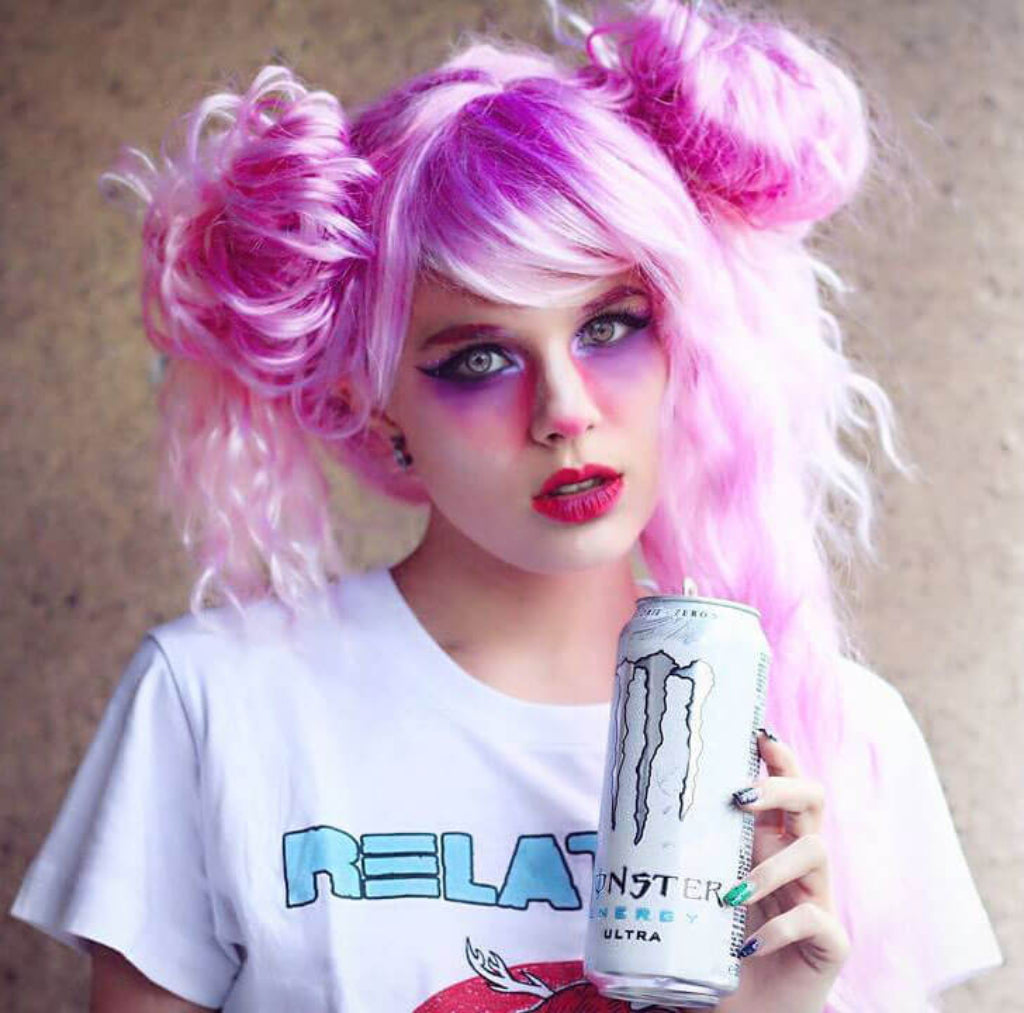 Person with pink hair and colorful makeup holding a Monster Energy Ultra can.