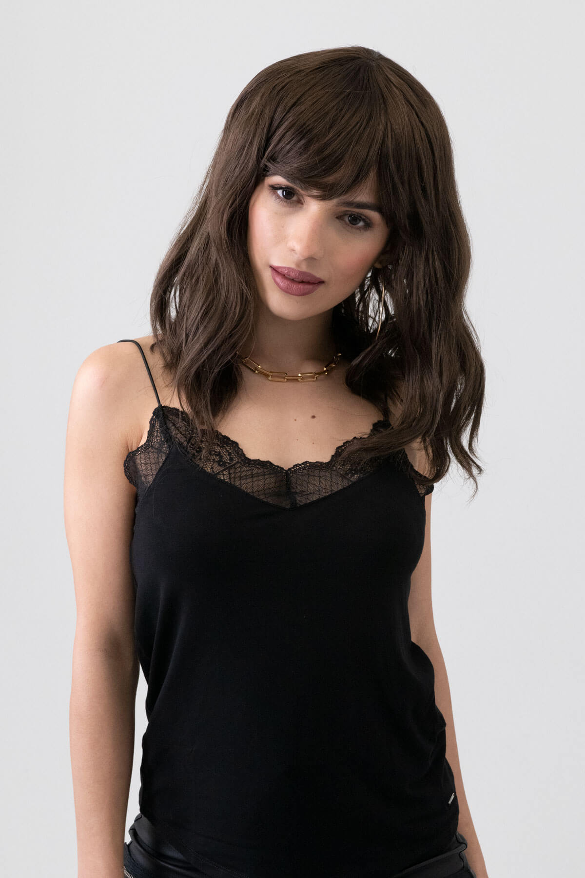 Woman wearing a black lace-trimmed top against a white background. Long brown wavy bob (lob) wig: Lottie