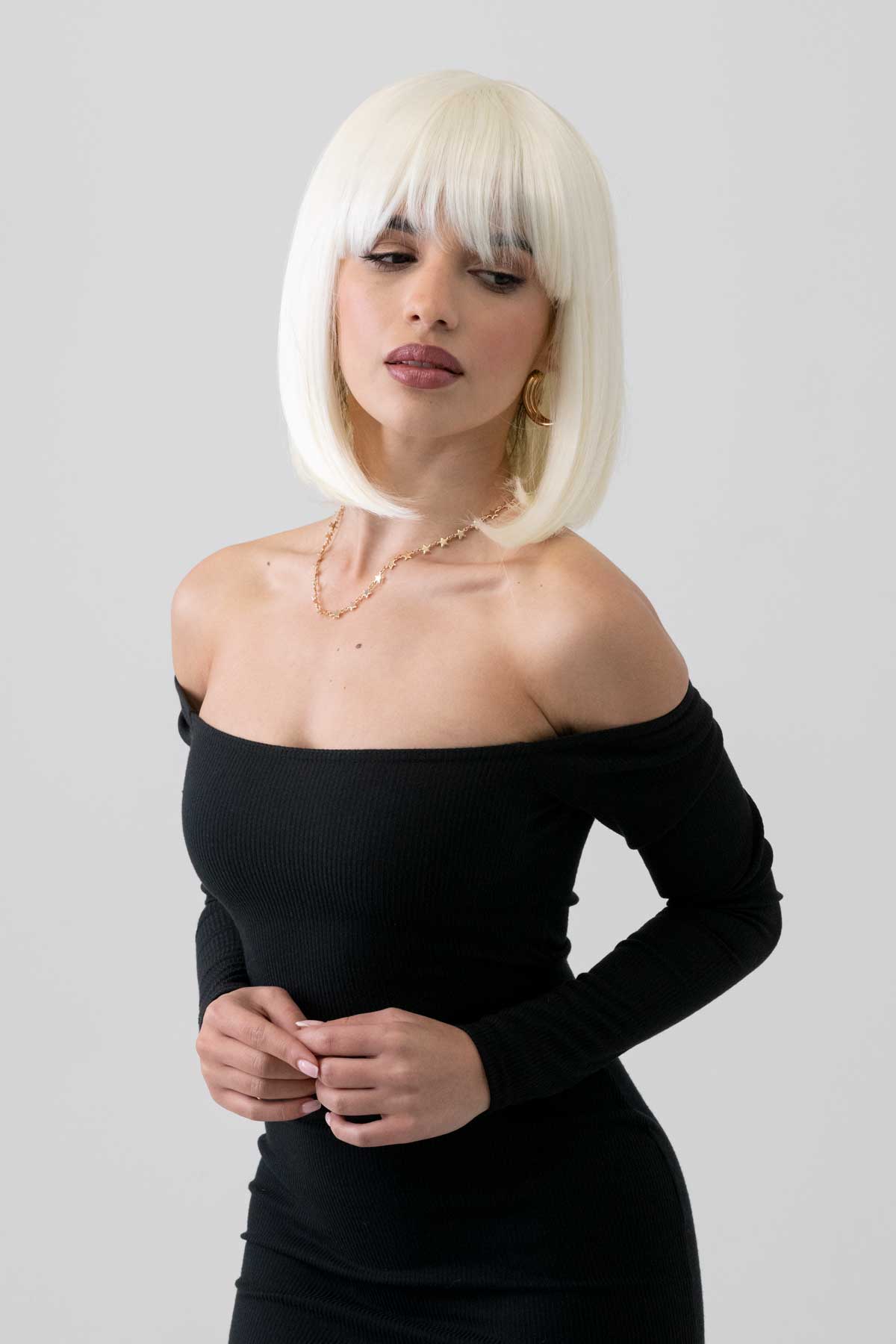 Woman with platinum blonde hair wearing a black off-shoulder dress with a plain background. Platinum blonde bob wig, shoulder length: Neve