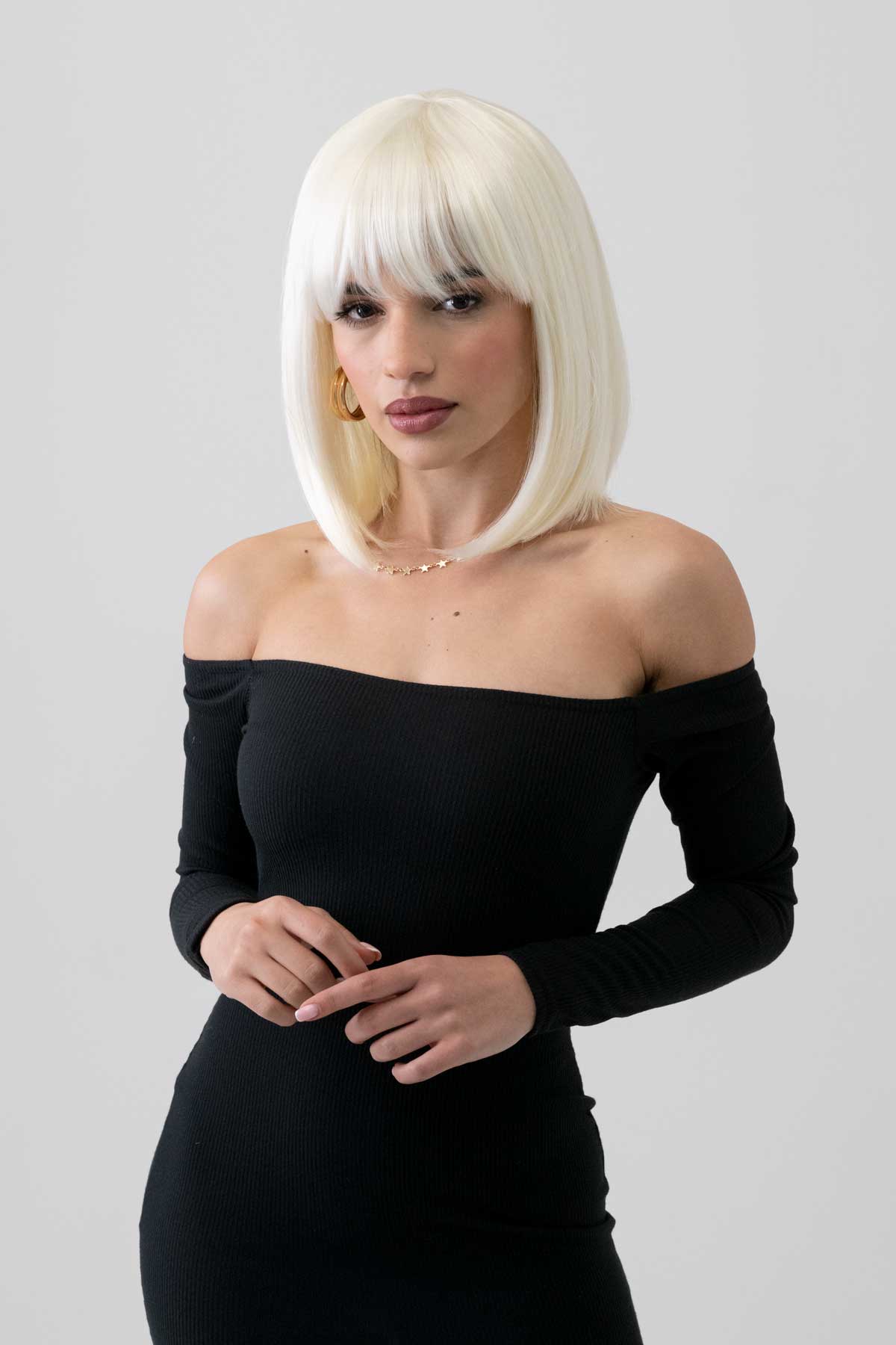 Woman with platinum blonde hair wearing a black off-shoulder dress with a plain background. Platinum blonde bob wig, shoulder length: Neve